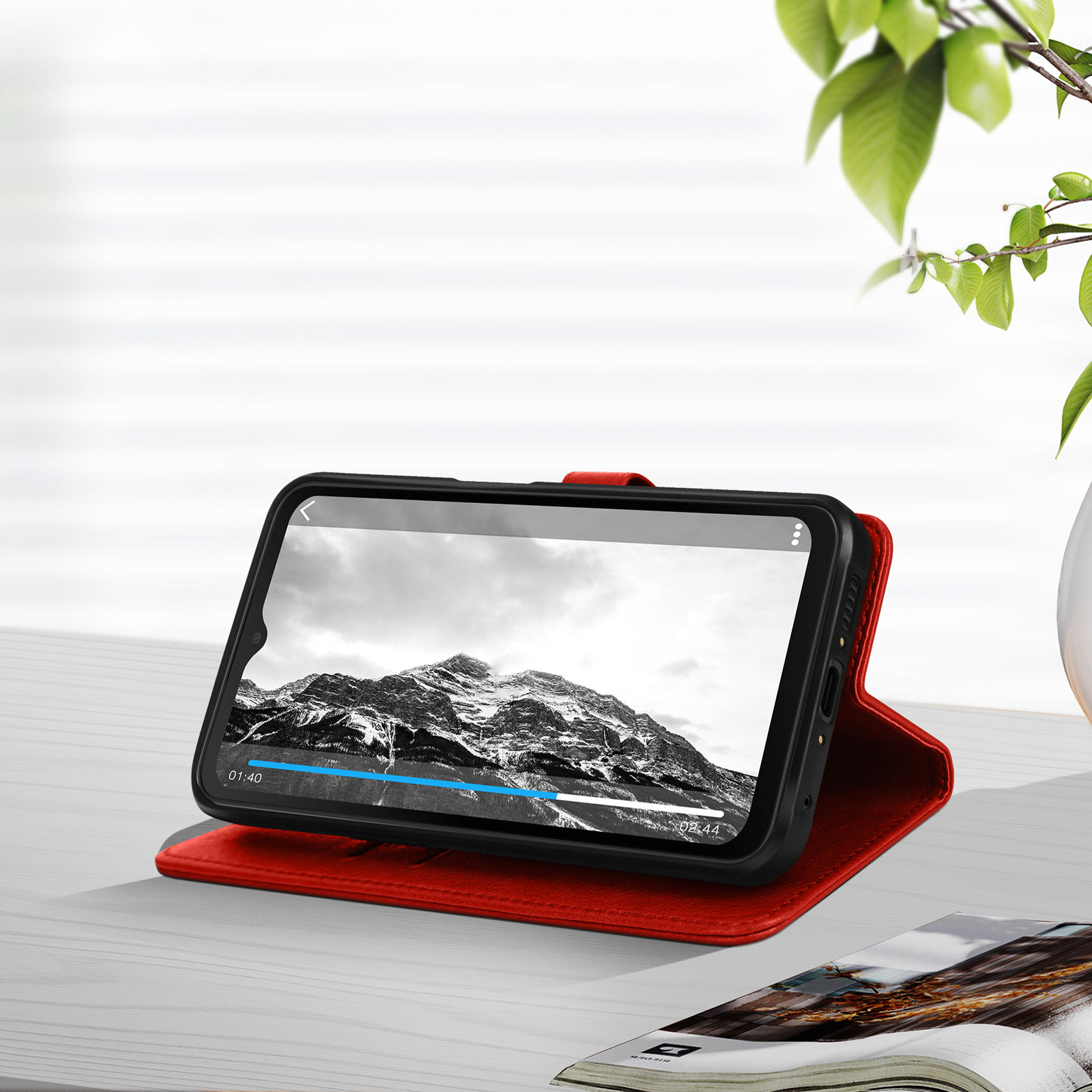 Un smartphone à l'intérieur d'un étui rouge, calé pour regarder une vidéo. Un magazine est au premier plan.