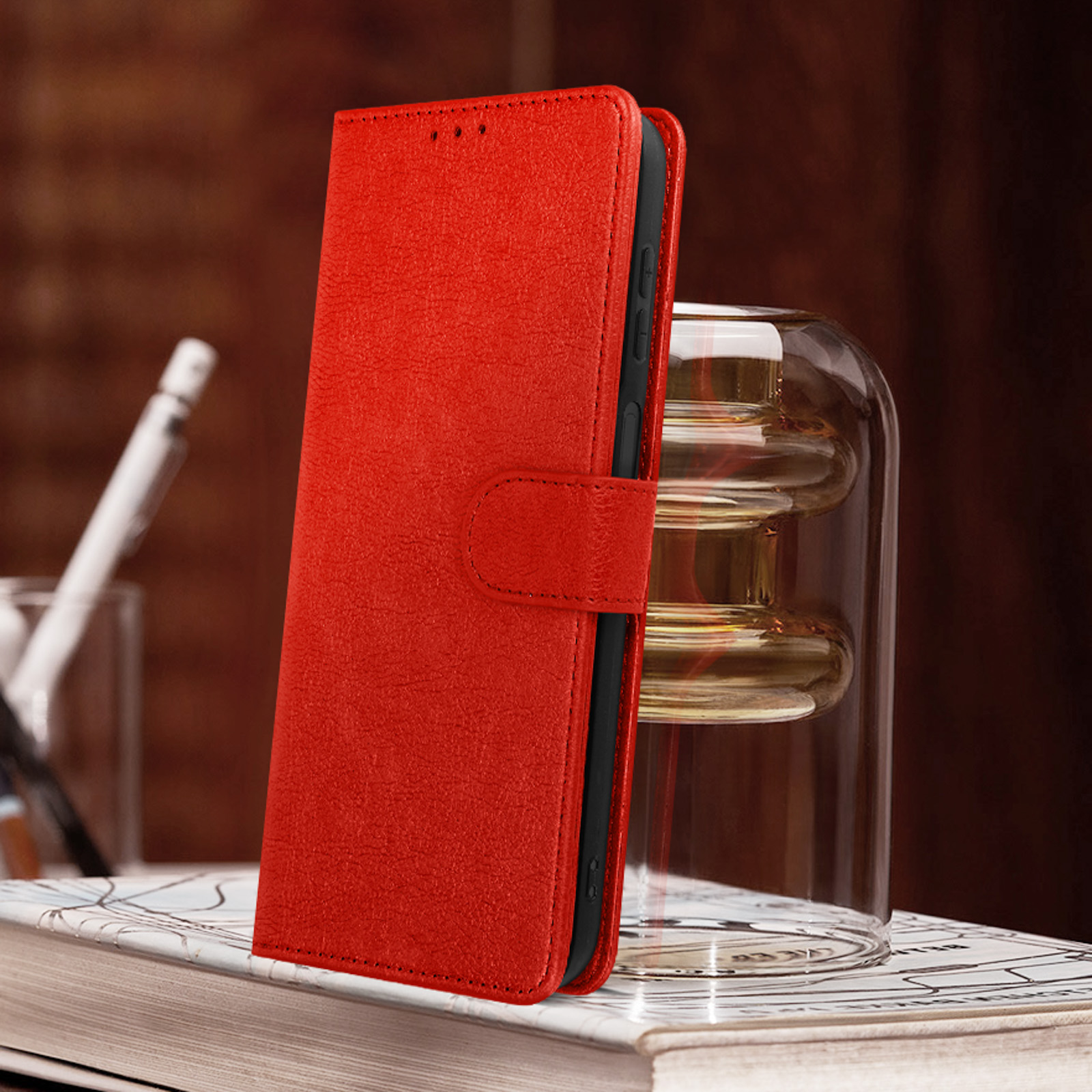 Étui de téléphone en cuir rouge sur un livre. Fond : verre et surface en bois.