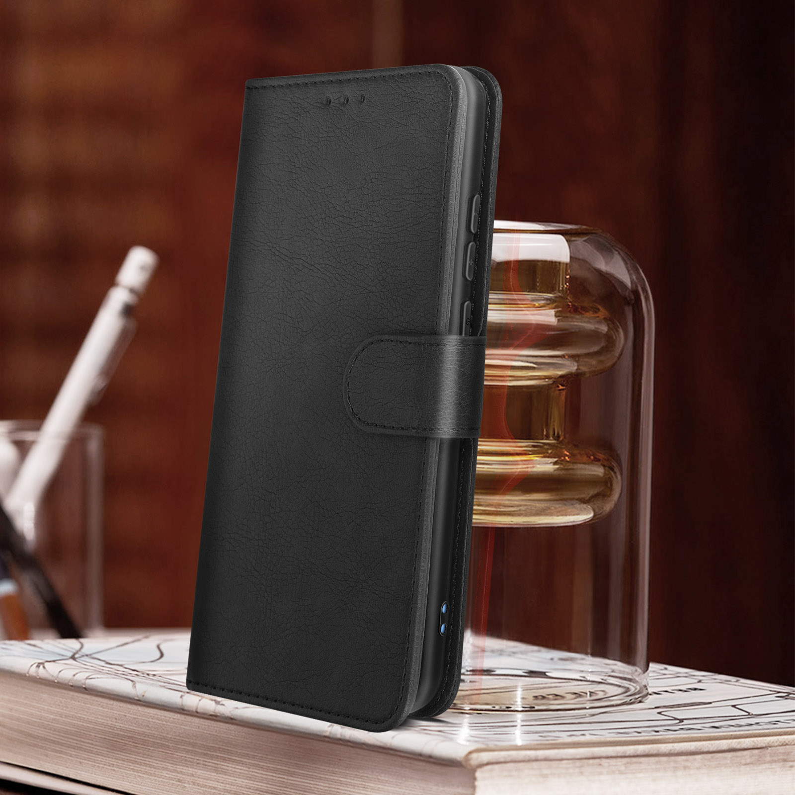 Custodia per telefono in pelle nera, chiusa, con chiusura a bottone, su legno e vaso.