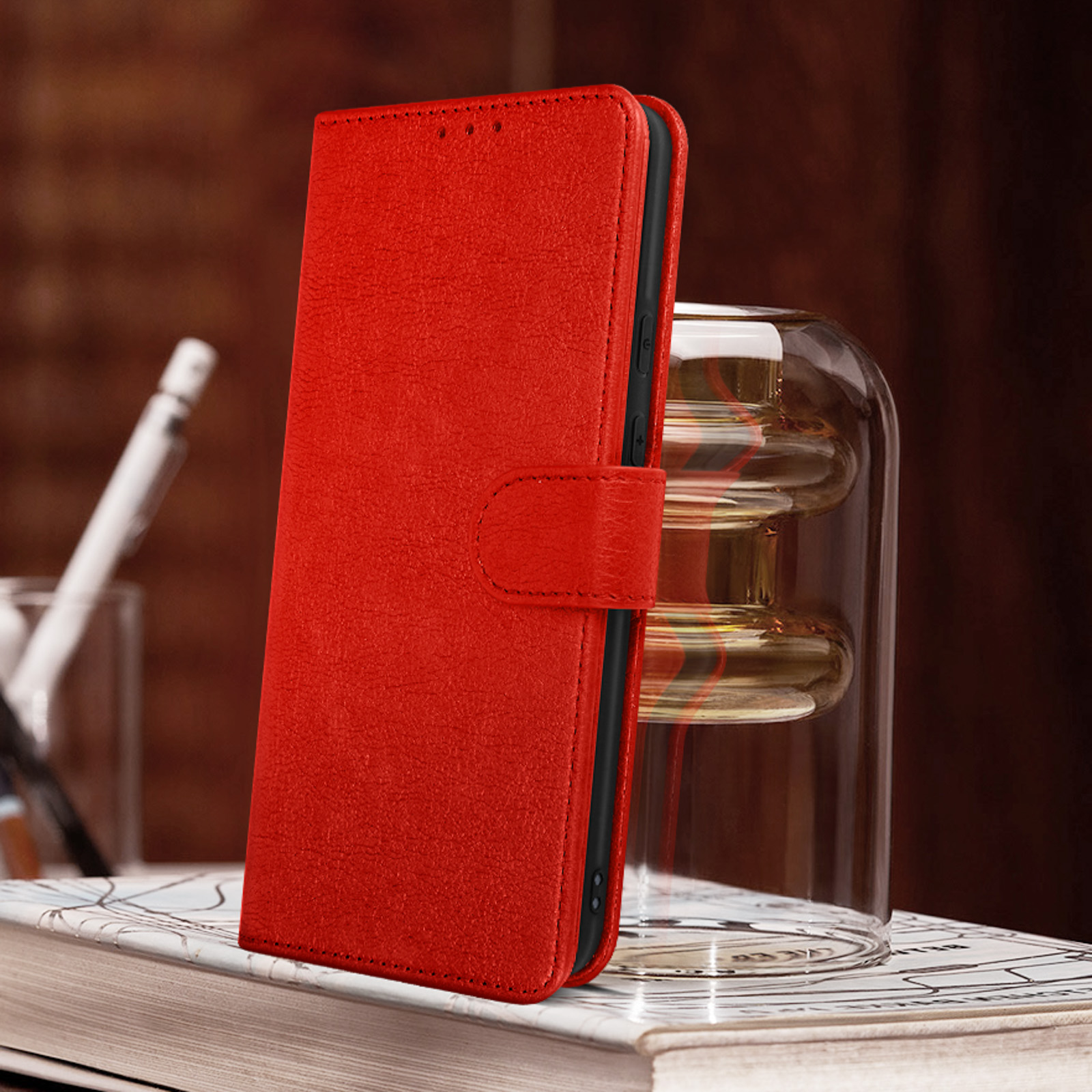 Étui de téléphone en cuir rouge, fermé, sur une surface en bois. Il y a un bocal en verre derrière.