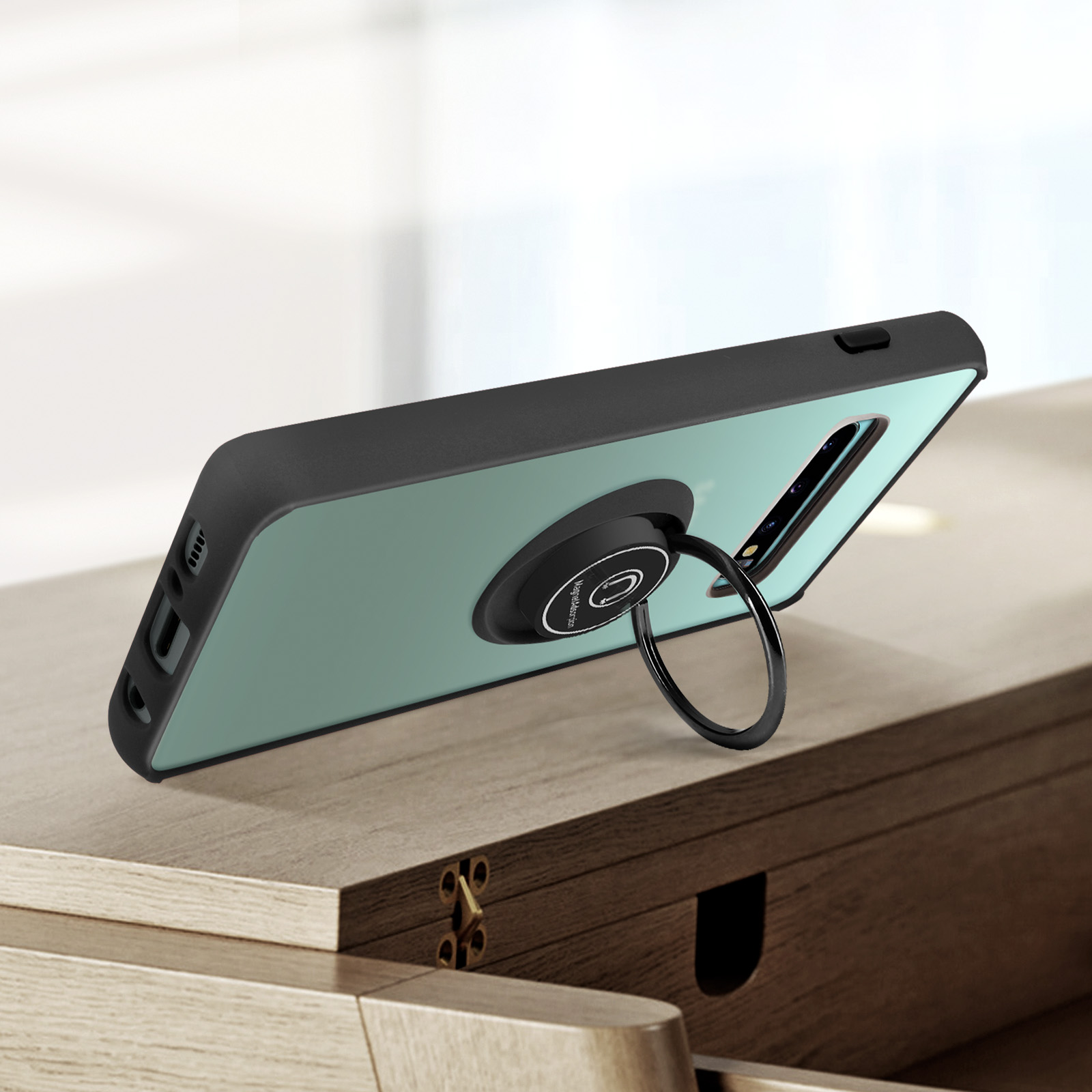 Custodia per telefono nera con supporto ad anello. Il telefono è verde e appoggiato su legno.