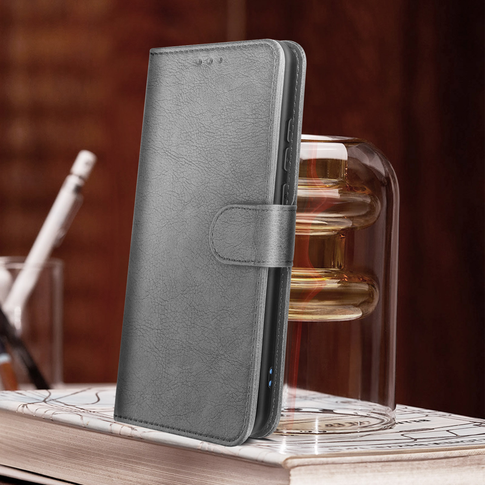 Graue Leder-Handyhülle. Die Hülle ist offen und zeigt das Telefon. Glasvase und Bleistift im Hintergrund.