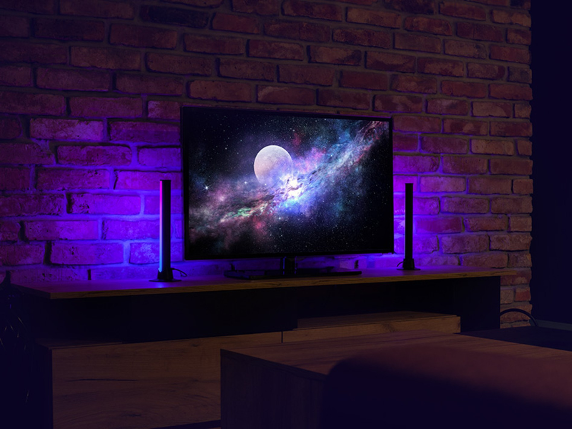 Pokój z telewizorem na drewnianej szafce, z dwoma pałeczkami świetlnymi po każdej stronie. Tło ściany z cegieł.