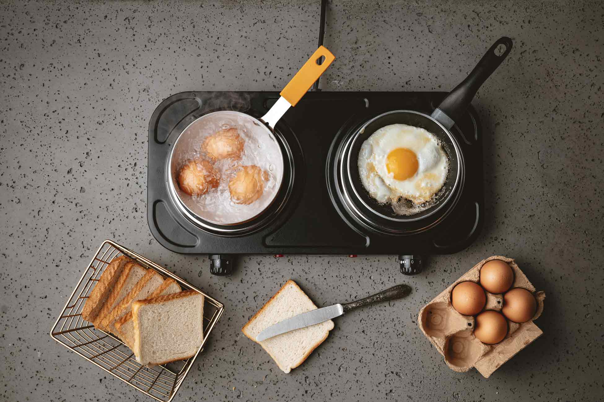 Jajka gotujące się w garnku, jajko sadzone, chleb i jajka w kartonie na szarej powierzchni.