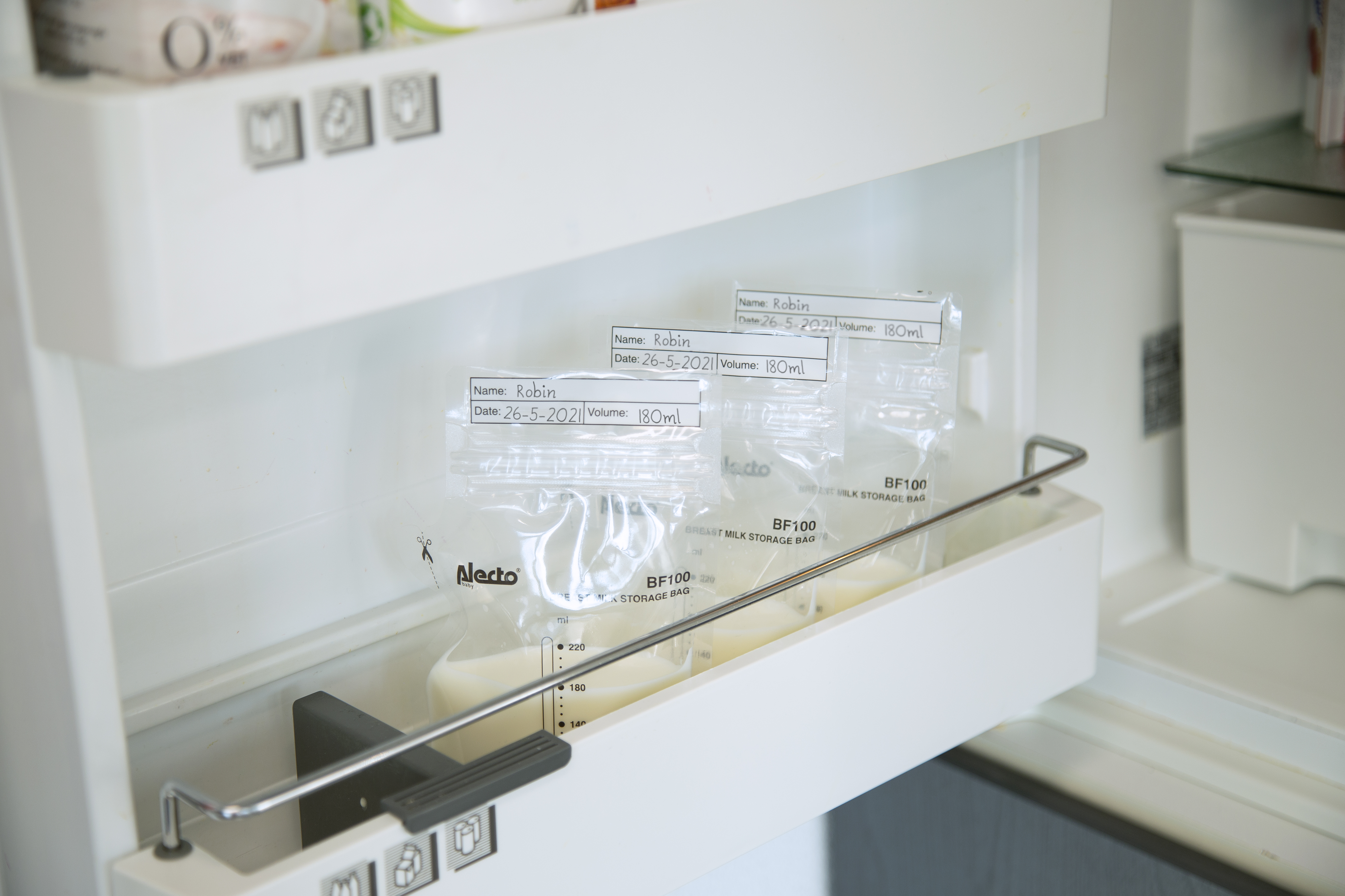 Breast milk bags in a refrigerator drawer. Bags are labeled with names, date, and volume.