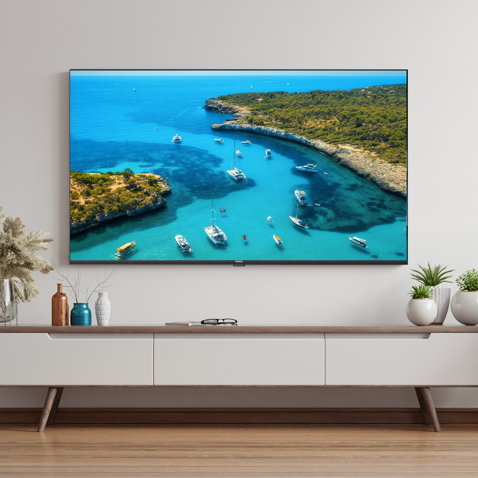 La TV mostra una baia con barche. Un mobile bianco con decorazioni e pavimento in legno è davanti alla TV.