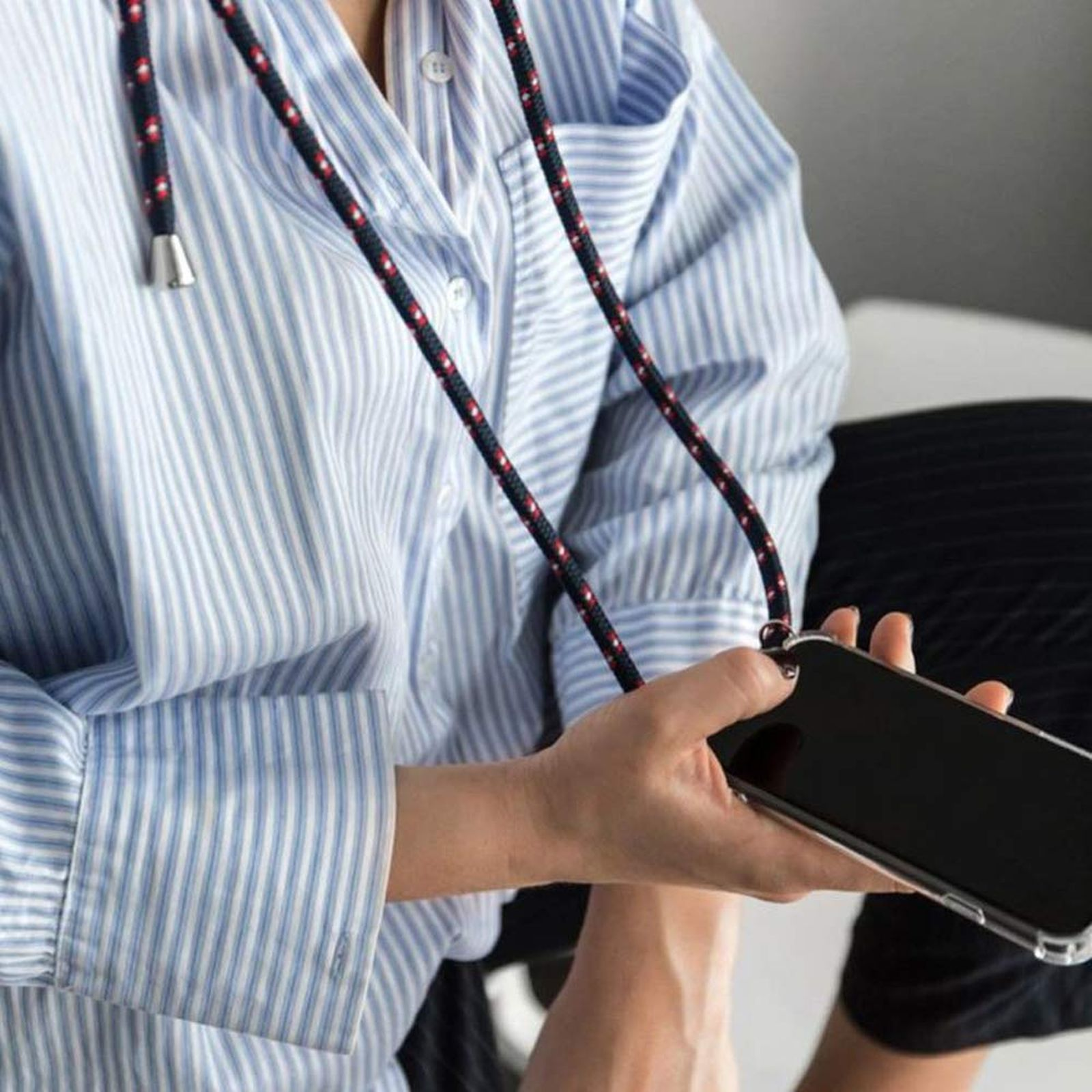 Person hält ein Telefon mit einem Schlüsselband. Das Telefon ist schwarz, das Schlüsselband rot und blau.
