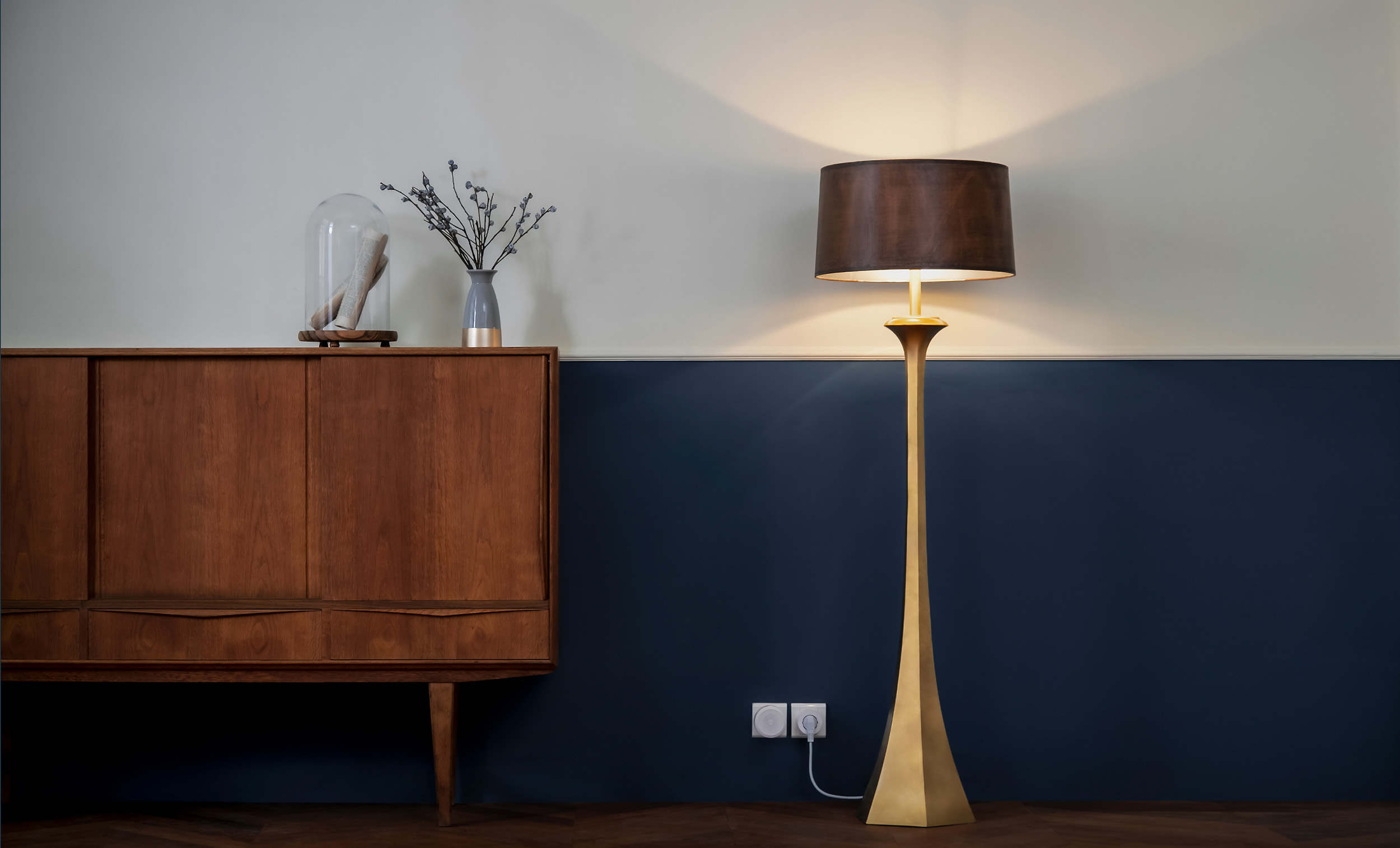 Eine moderne Stehlampe mit dunklem Lampenschirm steht in der Nähe eines Holzschranks vor einer zweifarbigen Wand.