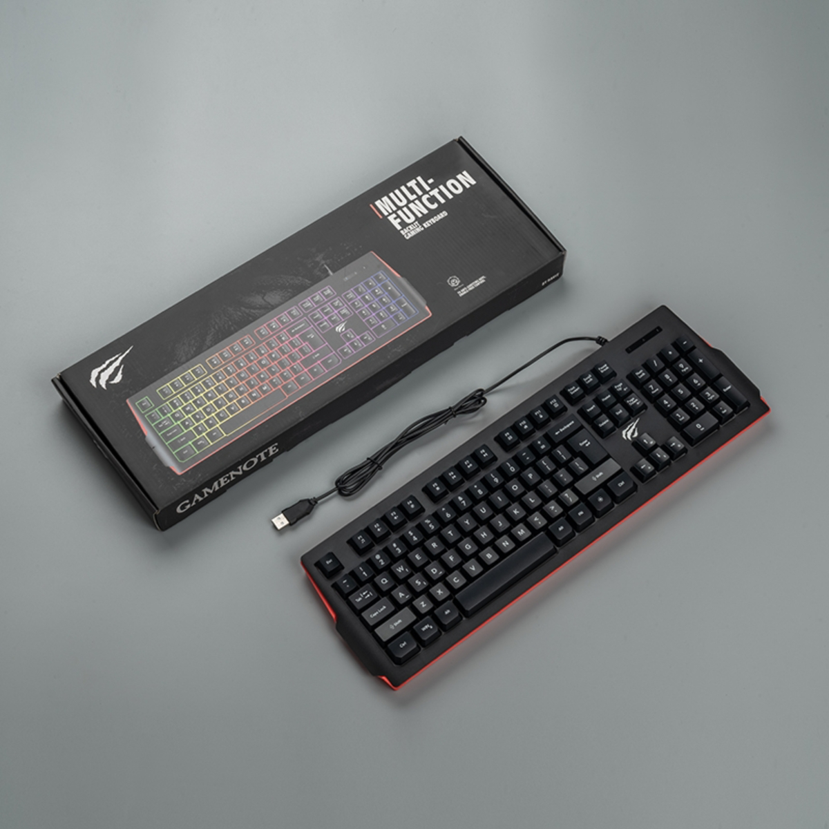 Teclado y caja negros, con un cable USB. La caja dice 'MULTI-FUNCTION'. Fondo gris.
