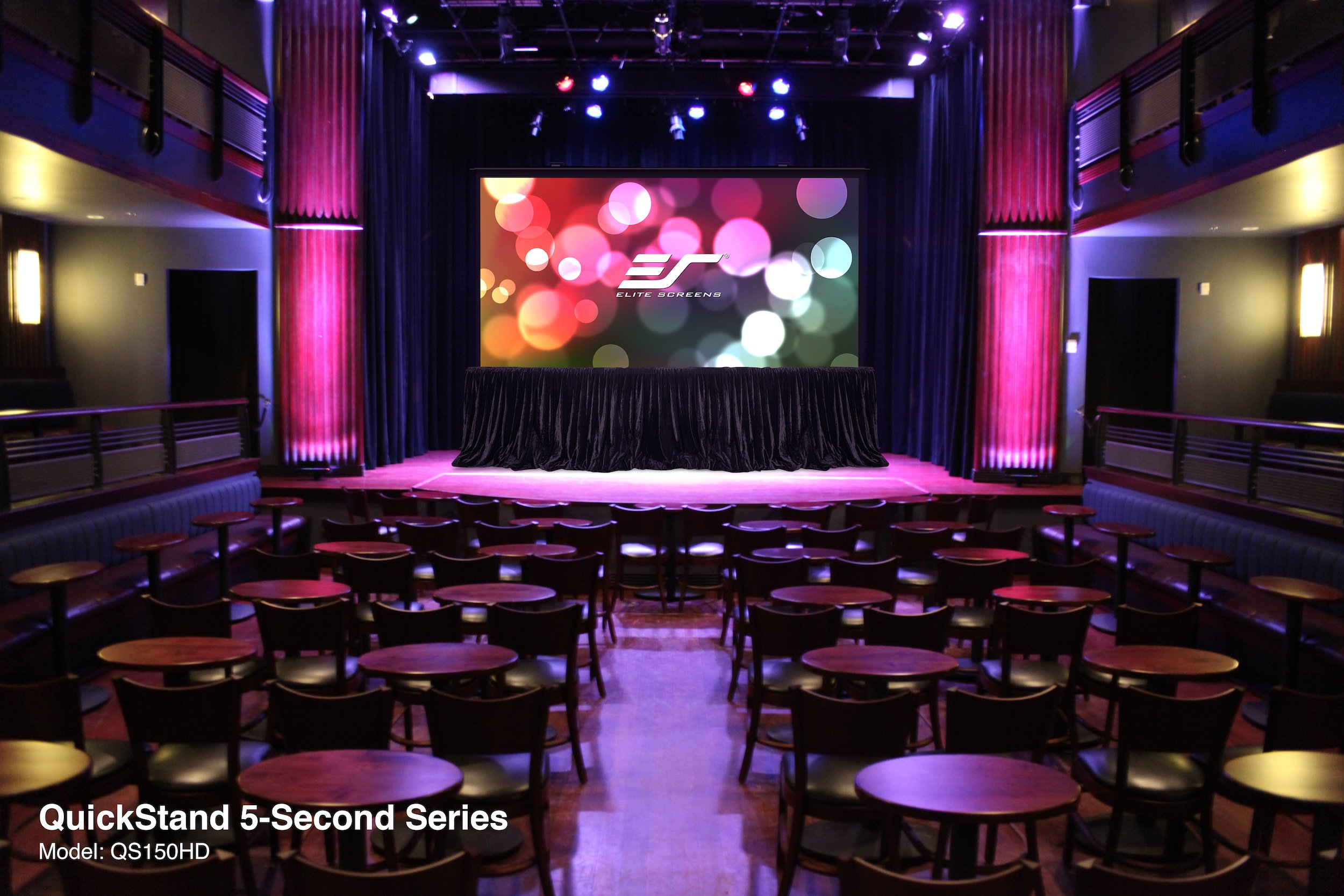 Inside a theater. There is a stage with a screen displaying a colorful image.
