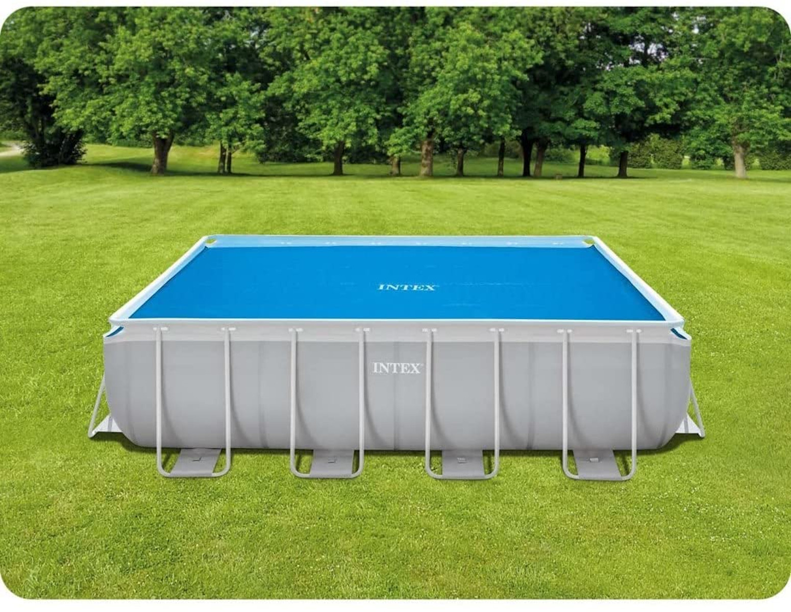 Piscina rettangolare con acqua blu, coperta con un telone blu, in un campo verde.