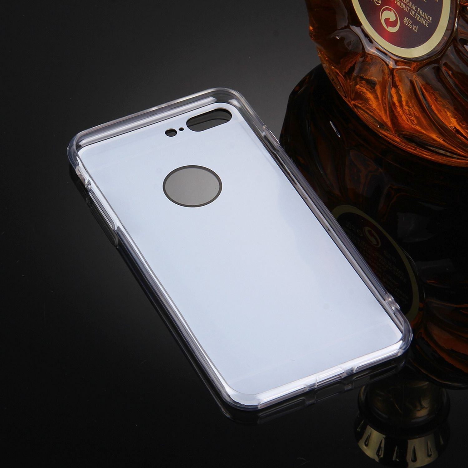 Eine transparente Handyhülle auf schwarzem Untergrund. Eine Cognacflasche befindet sich im Hintergrund.