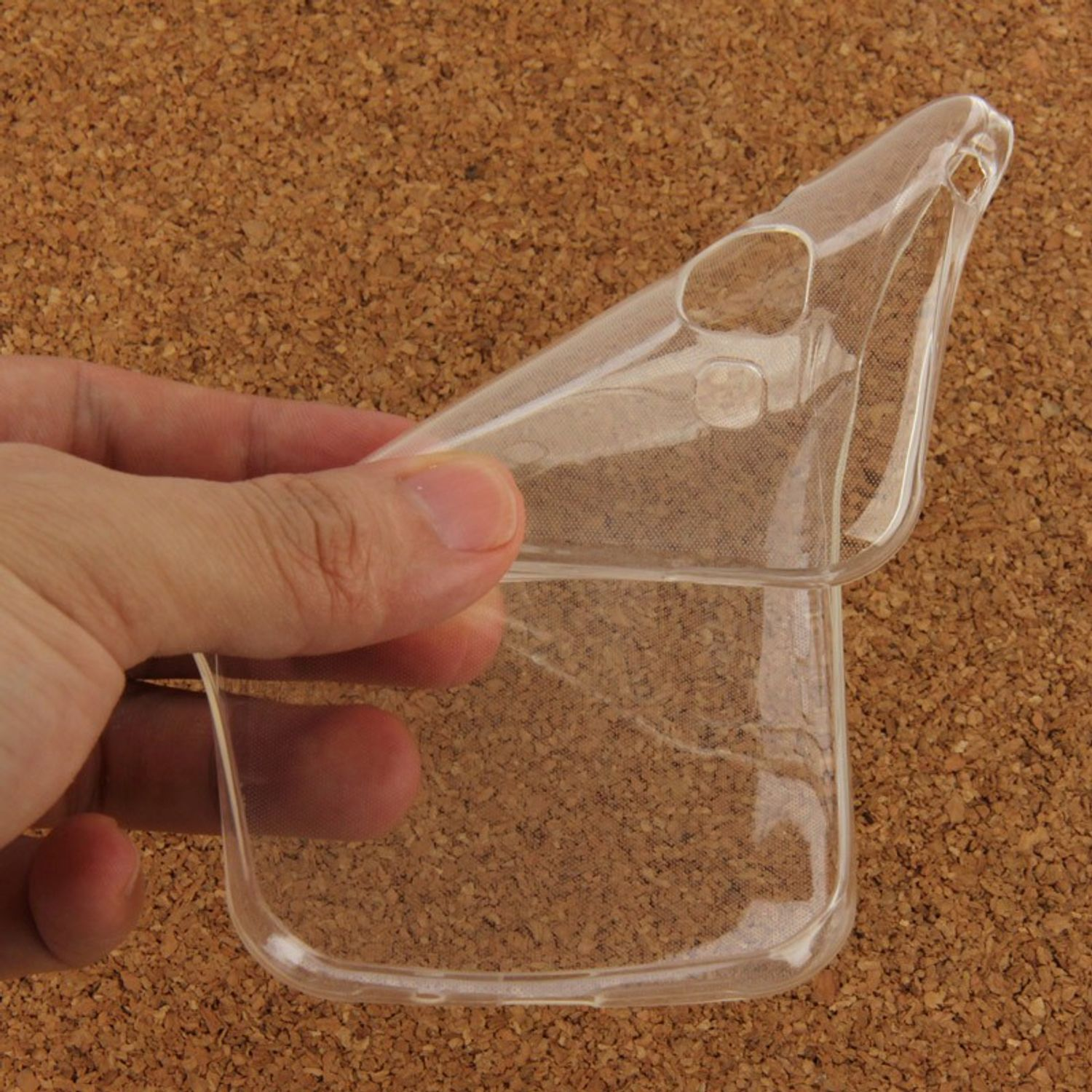 Klare Plastik-Handyhülle, von Hand auf Korktafel gehalten. Gehäuse ist gebogen.