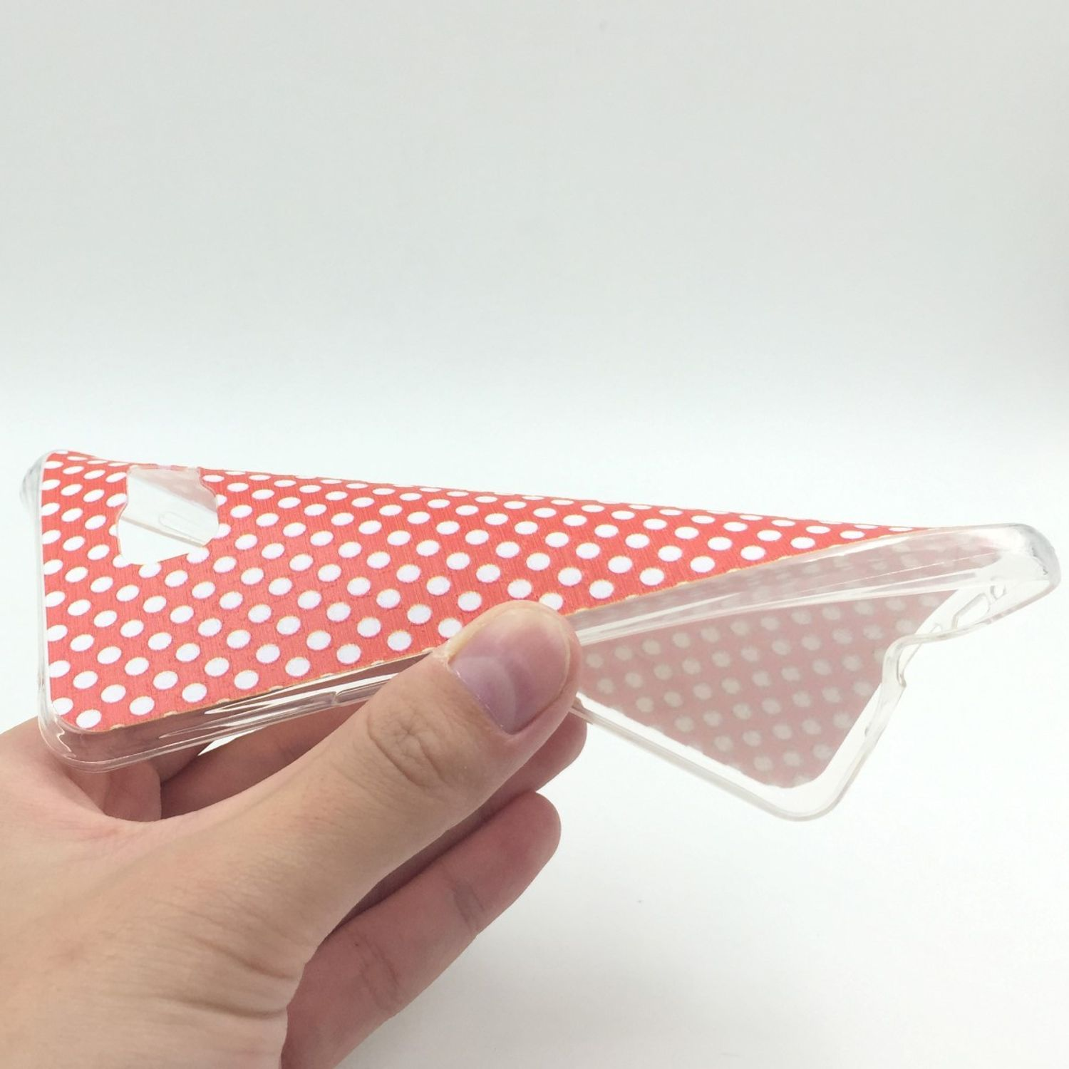 Hand hält eine transparente Handyhülle mit rot-weißem Polka-Dot-Design.