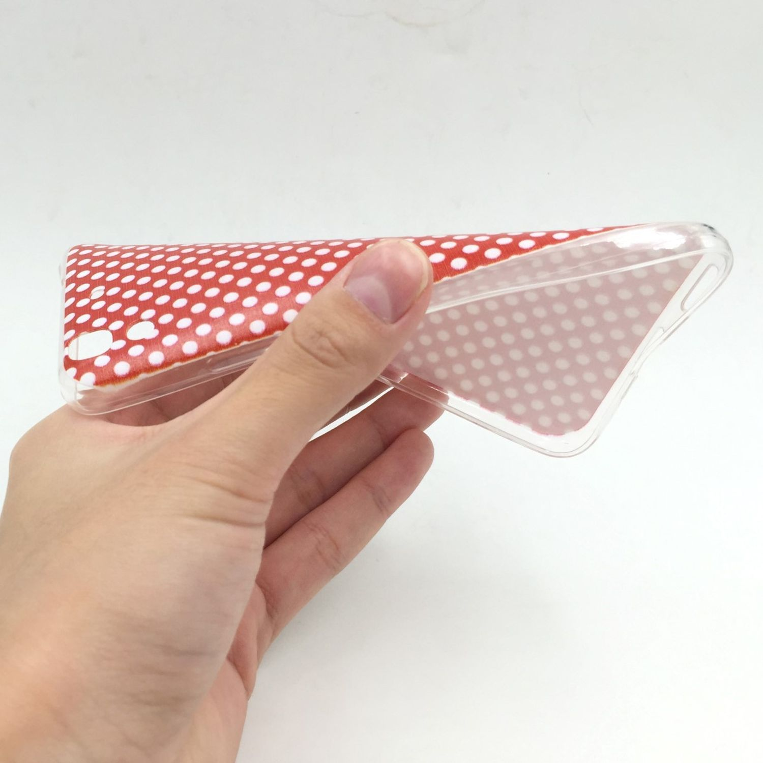Hand, die eine transparente Handyhülle mit einem roten Polka-Dot-Design im Inneren hält.