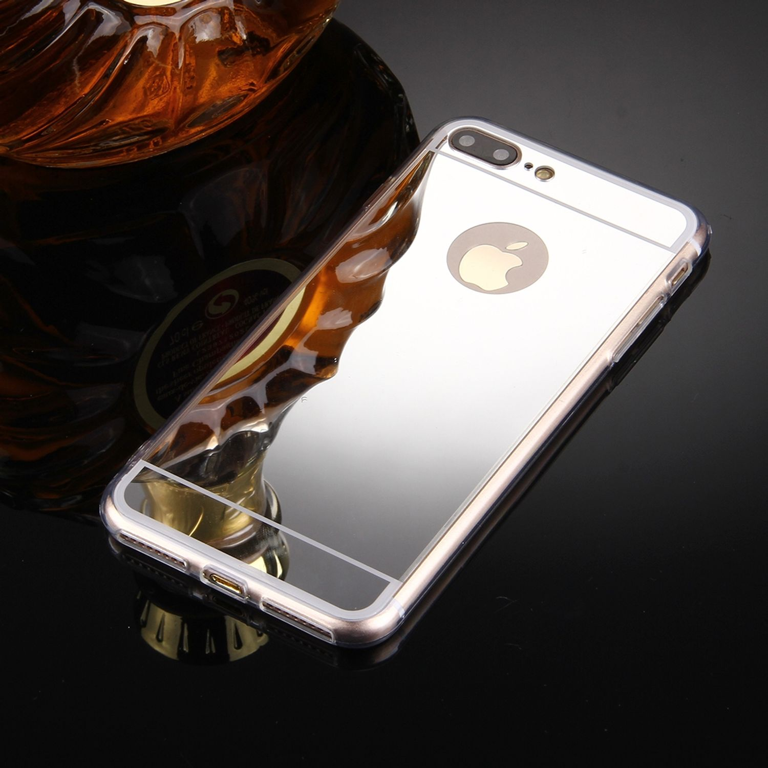 Eine reflektierende silberne Handyhülle auf einer reflektierenden schwarzen Oberfläche, mit einer Likörflasche im Hintergrund.