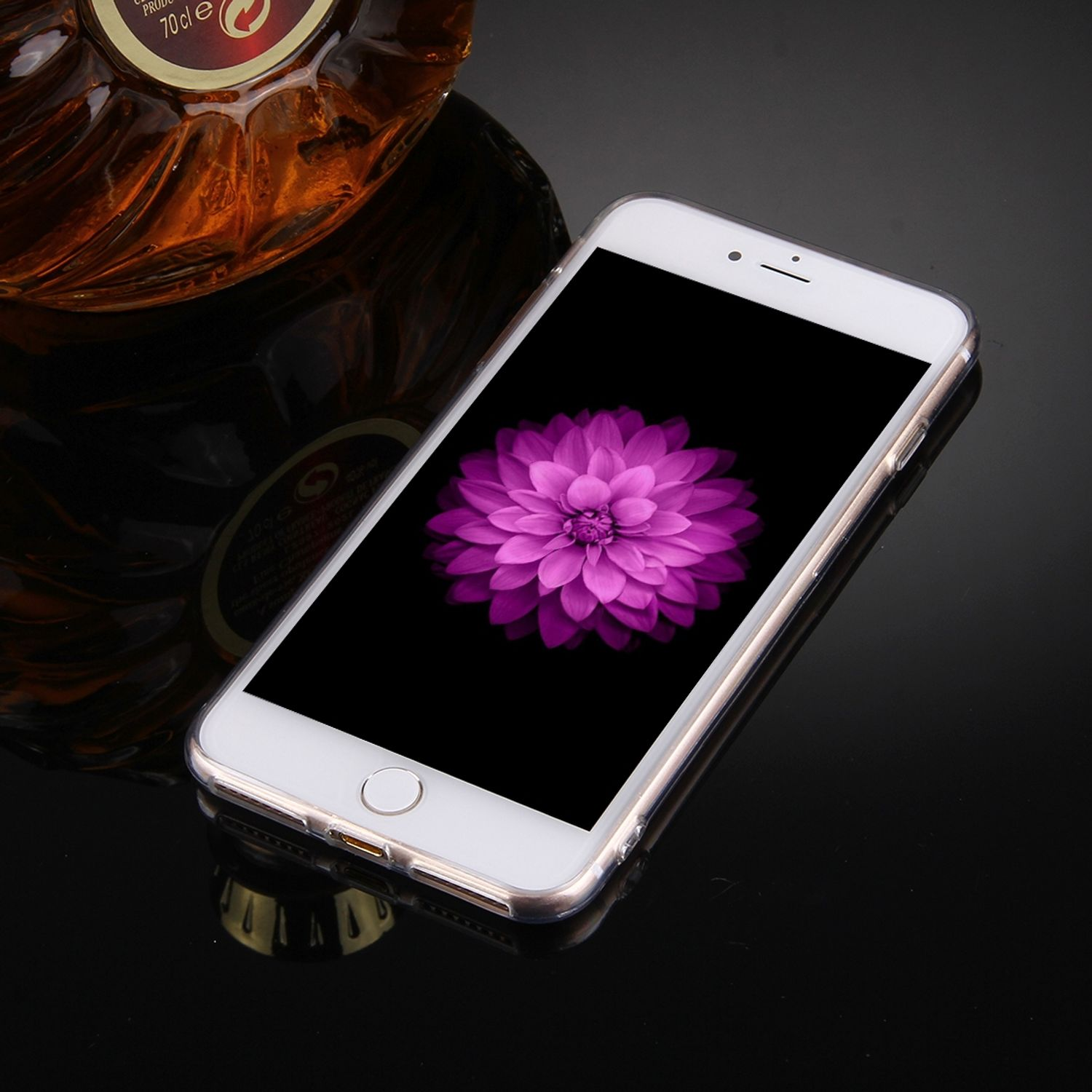 Telefon mit violetter Blume auf dem Bildschirm. Schwarzer Hintergrund. Eine Flasche im Hintergrund.