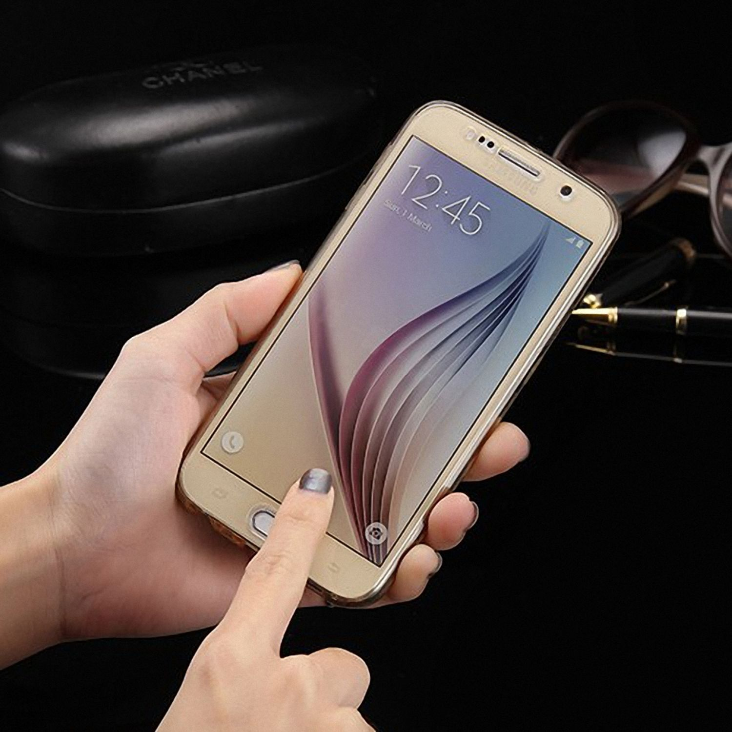 Ein goldenes Telefon in einer transparenten Hülle, das von einer Hand gehalten wird. Schwarzer Hintergrund, Sonnenbrille.
