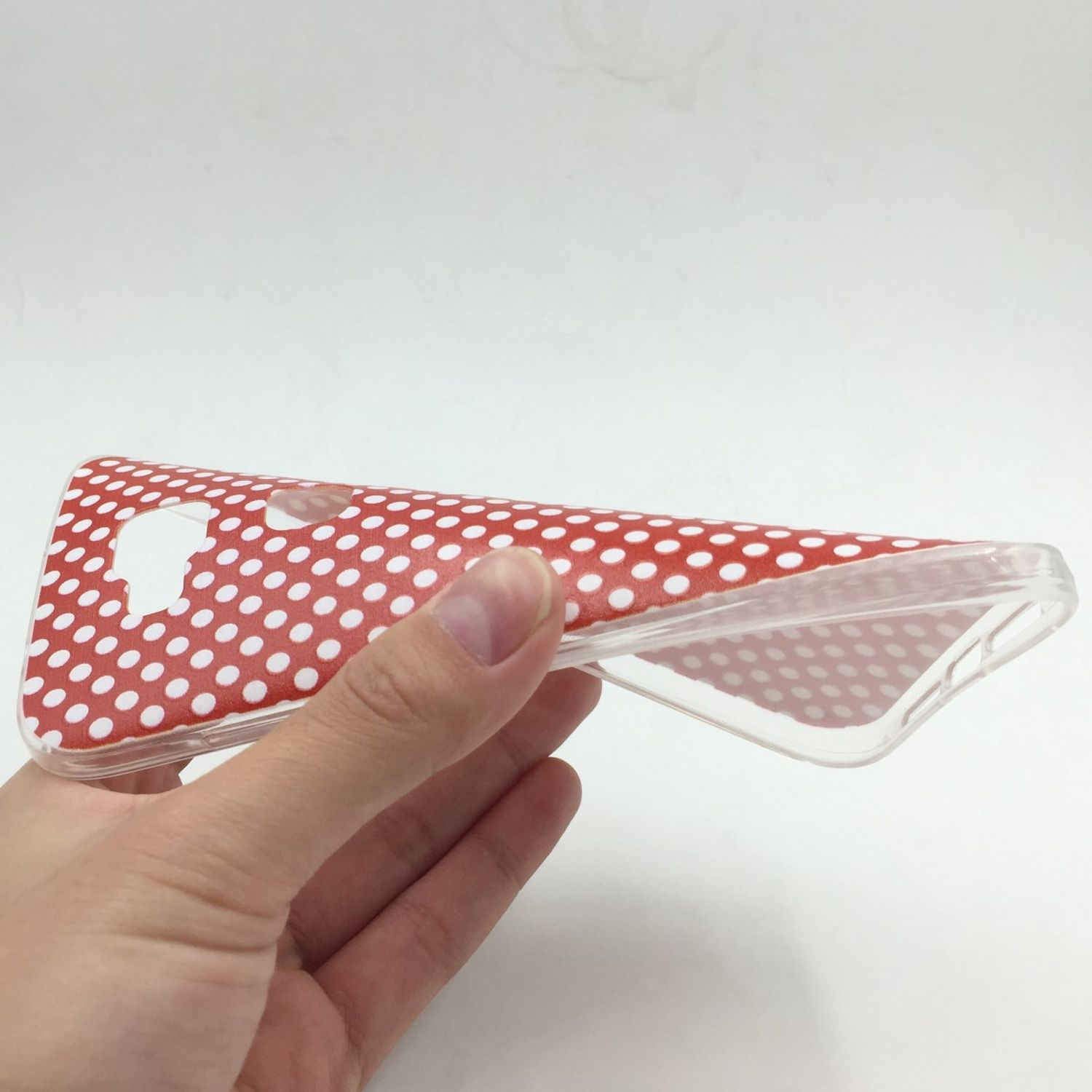 Hand hält eine transparente Handyhülle mit roten Punkten. Weißer Hintergrund.