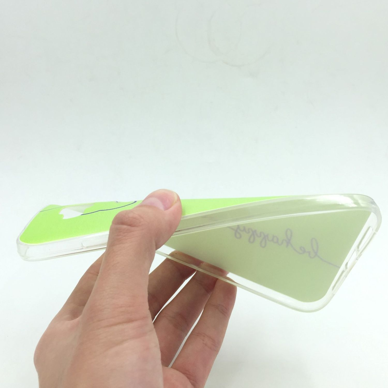 Hand hält transparente Handyhülle mit grün-weißem Design, weißer Hintergrund.