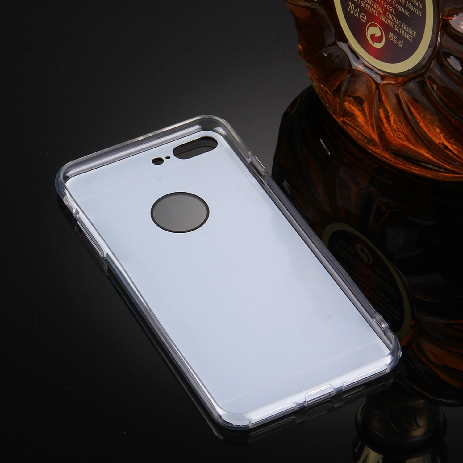 Transparente Handyhülle auf glänzender schwarzer Oberfläche, mit Cognac-Flasche im Hintergrund.