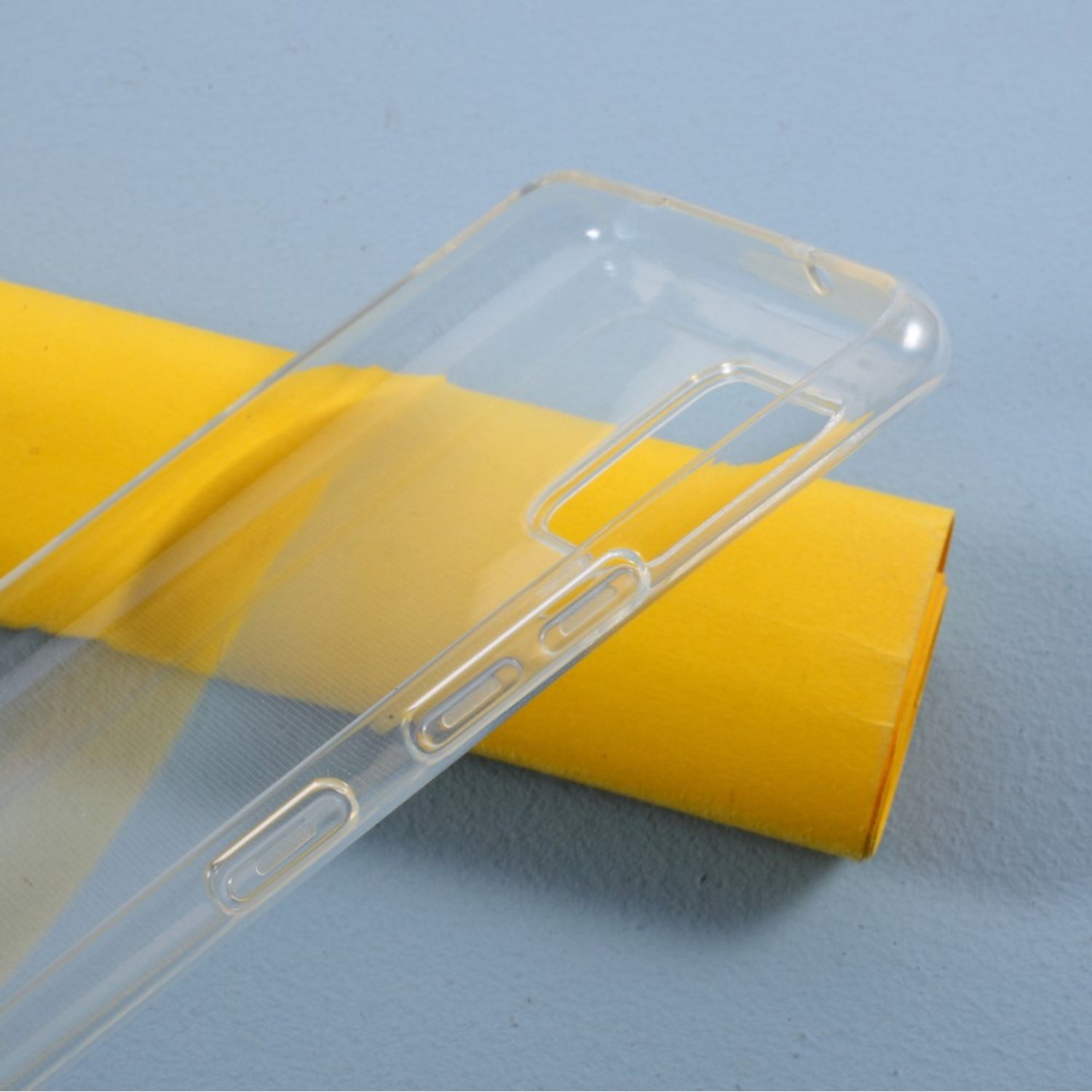 Transparente Handyhülle auf einer Oberfläche, mit einer Rolle gelben Papiers im Hintergrund.