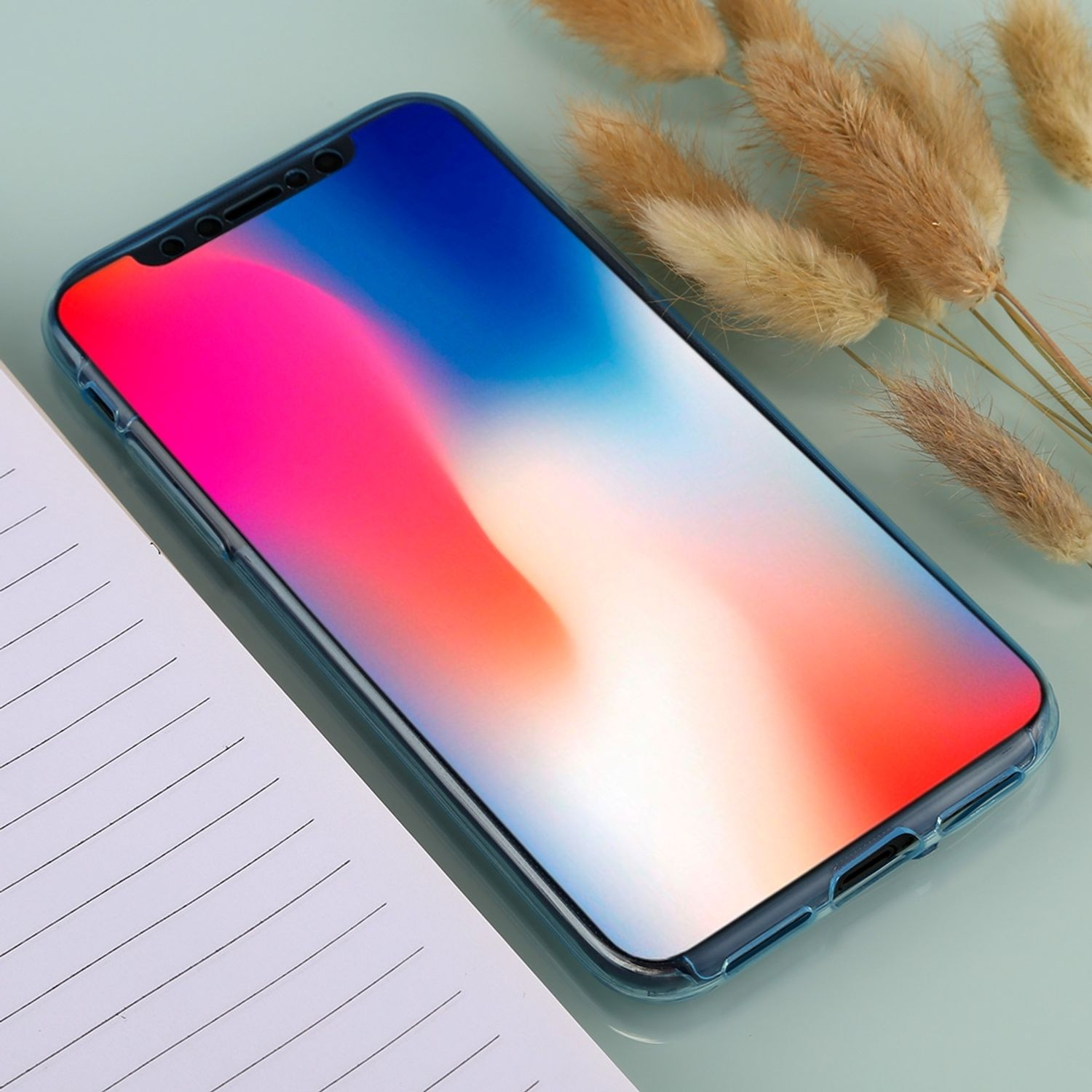 Smartphone mit blauem Gehäuse auf hellgrüner Oberfläche, mit Blumen und Notizblock.