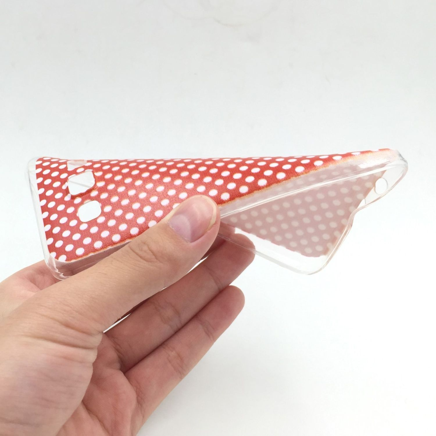 Hand hält transparente Handyhülle mit roten Tupfen. Weißer Hintergrund.