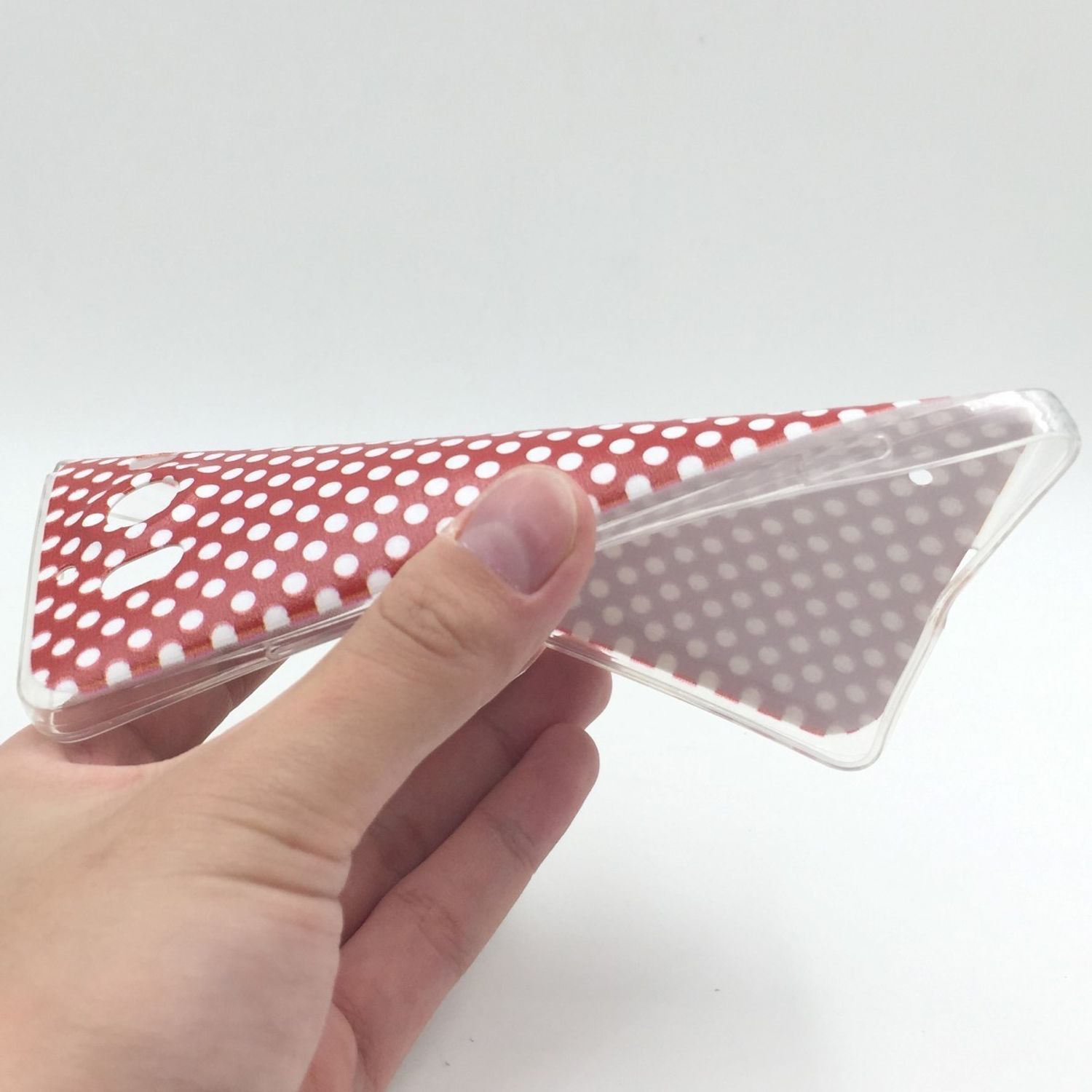 Hand hält eine Handyhülle mit rotem und weißem Tupfenmuster.