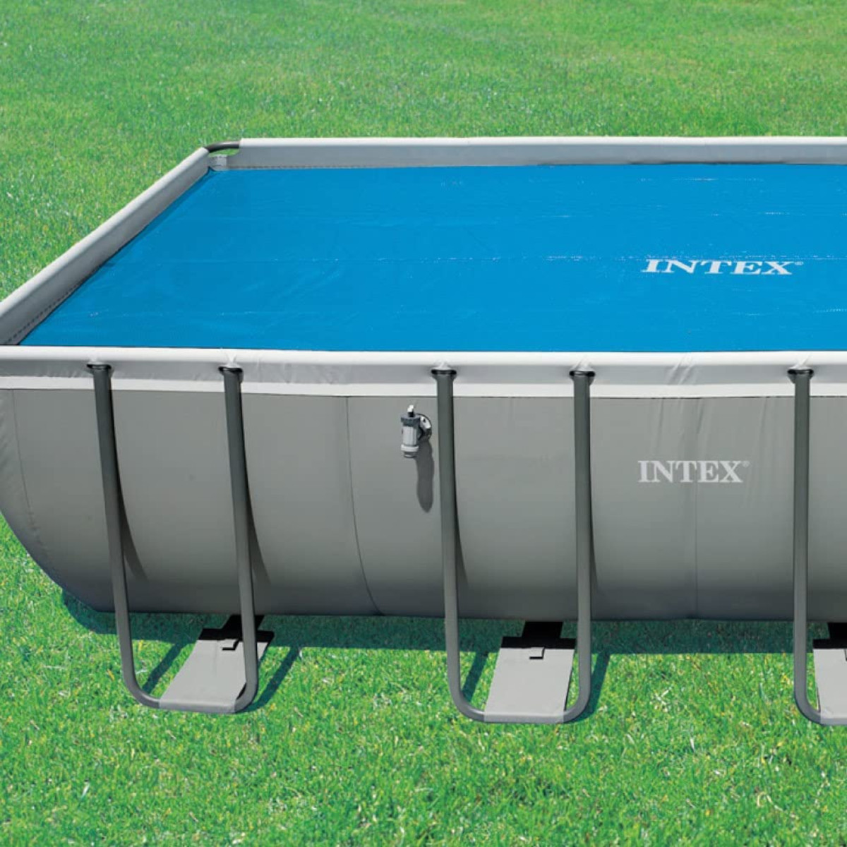 Ein rechteckiger Pool mit grauem Metallrahmen und blauer Abdeckung auf grünem Gras.
