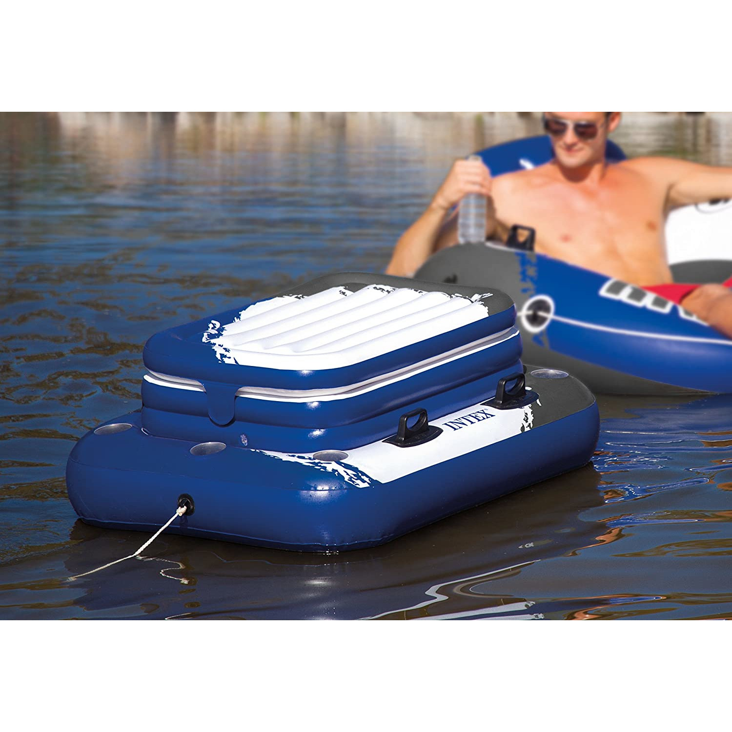 Blaues aufblasbares Floß auf dem Wasser, das einen Kühler hält. Eine andere Person ist im Hintergrund auf einem blauen Floß.