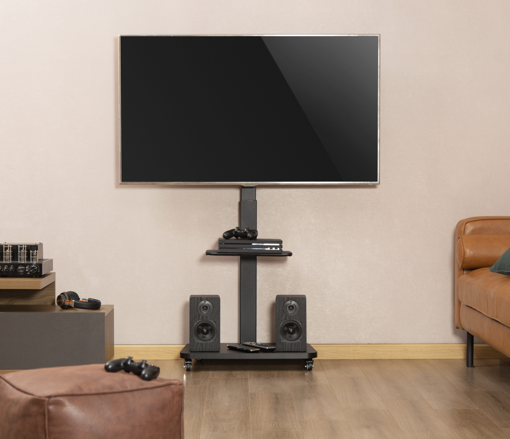 Fernseher auf Ständer mit Lautsprechern, Regal mit Konsole und Ledersitzhocker im Raum.