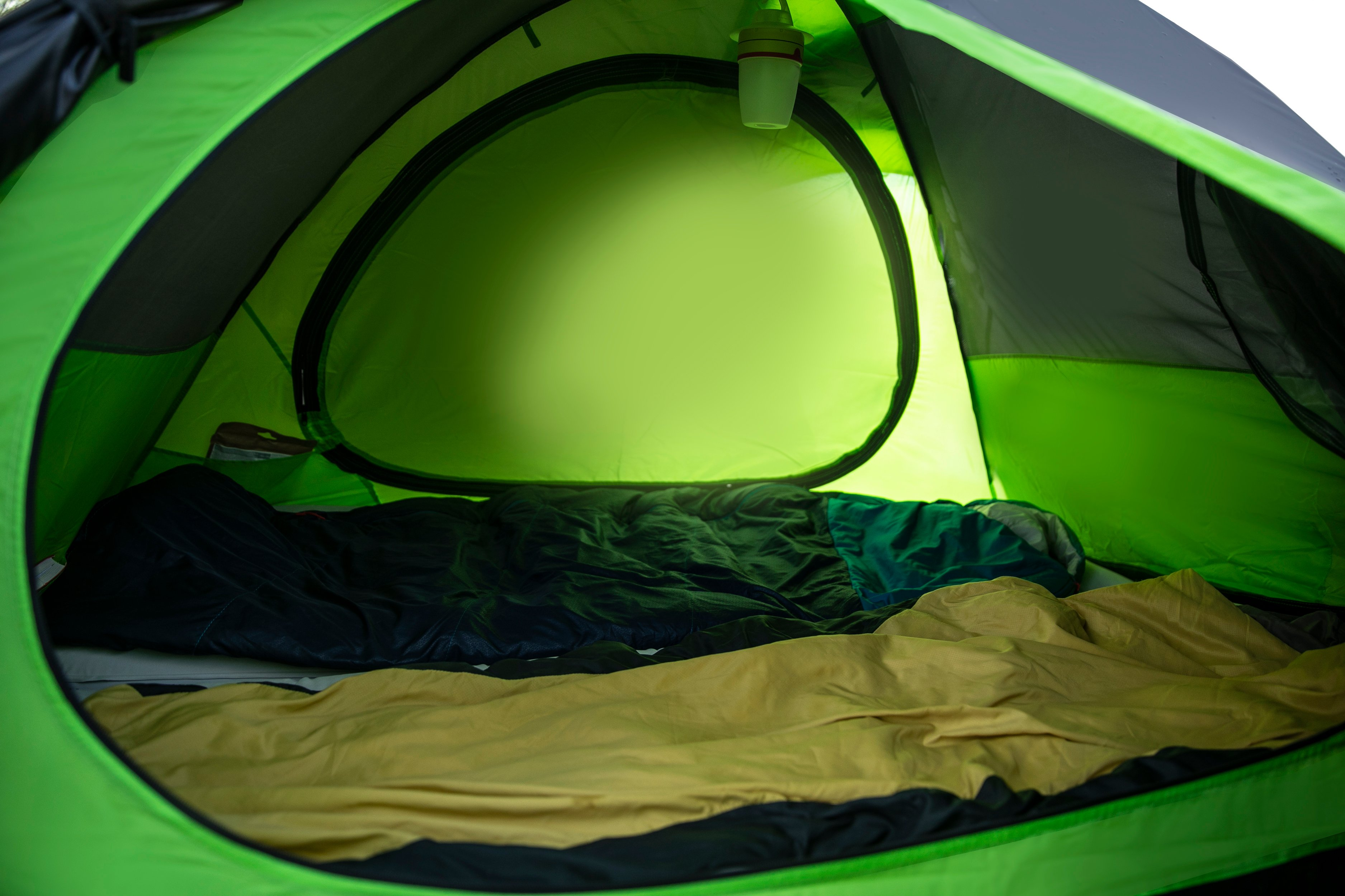 Dentro de una carpa verde y negra, se ven un saco de dormir y un colchón.
