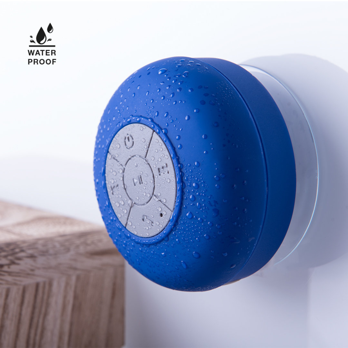 Altavoz azul impermeable con botones, en una pared blanca, con gotas de agua.