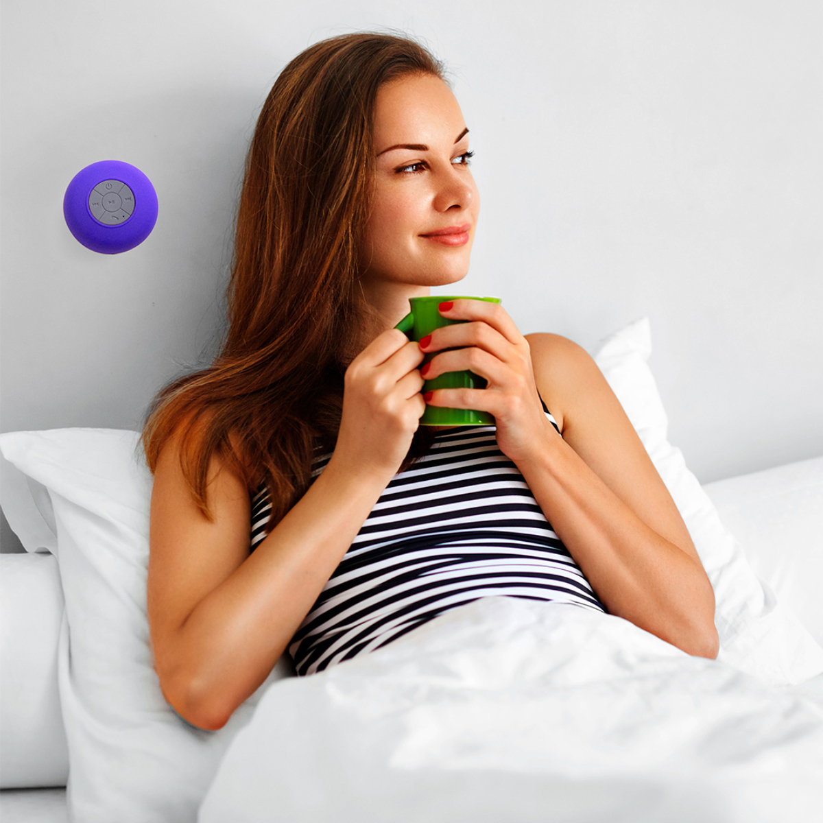 Mujer en la cama, sosteniendo una taza verde, con un altavoz morado montado en la pared.