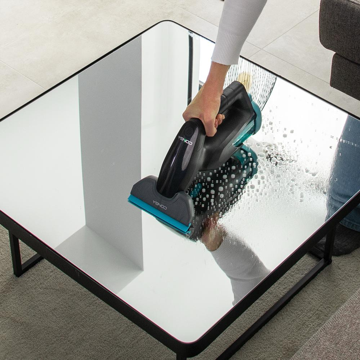 Osoba czyści błyszczący czarny stół płynem do mycia okien, widoczne są pęcherzyki.