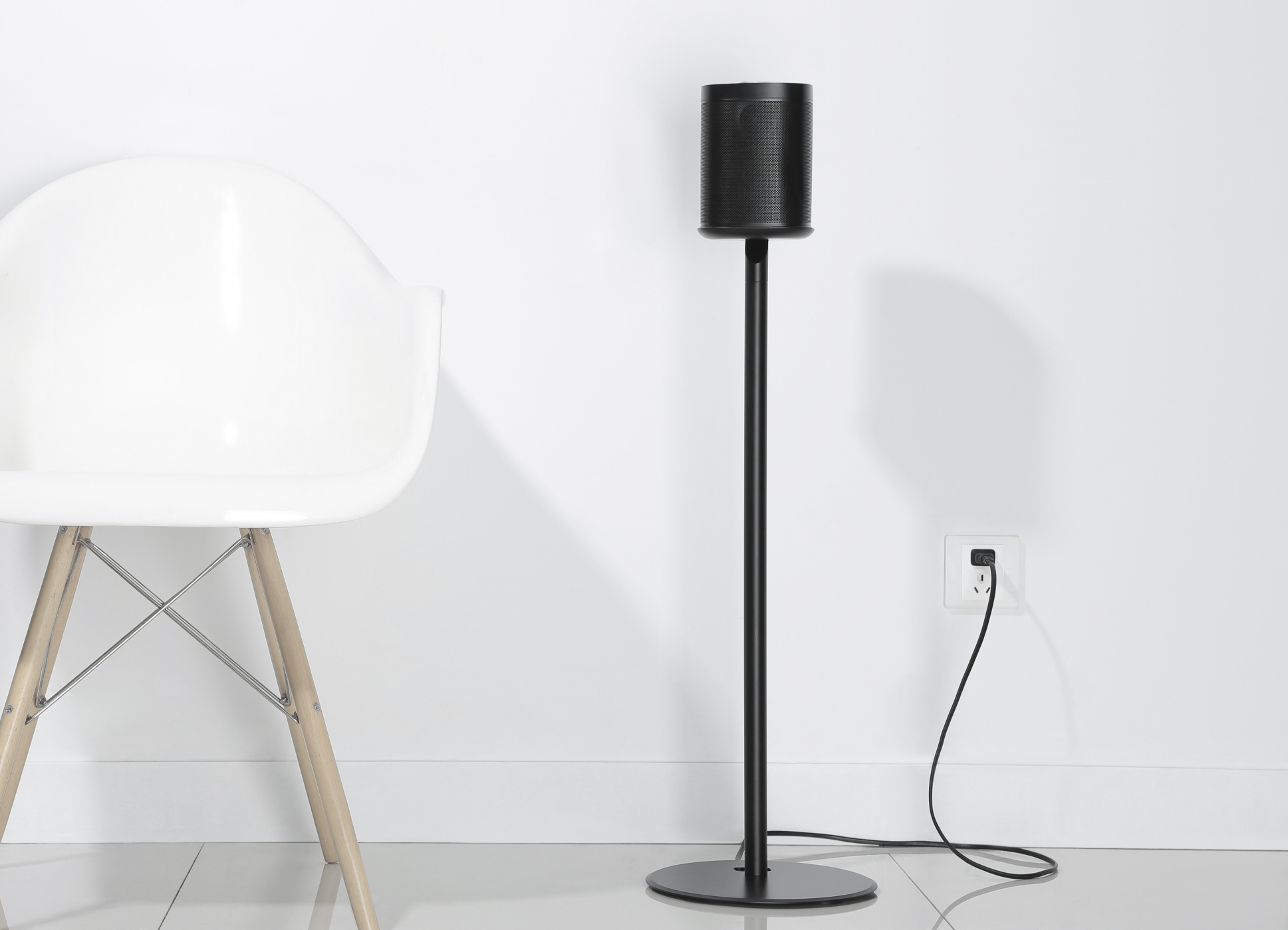 Zwarte speaker op standaard. Witte stoel en muur. Wit stopcontact.
