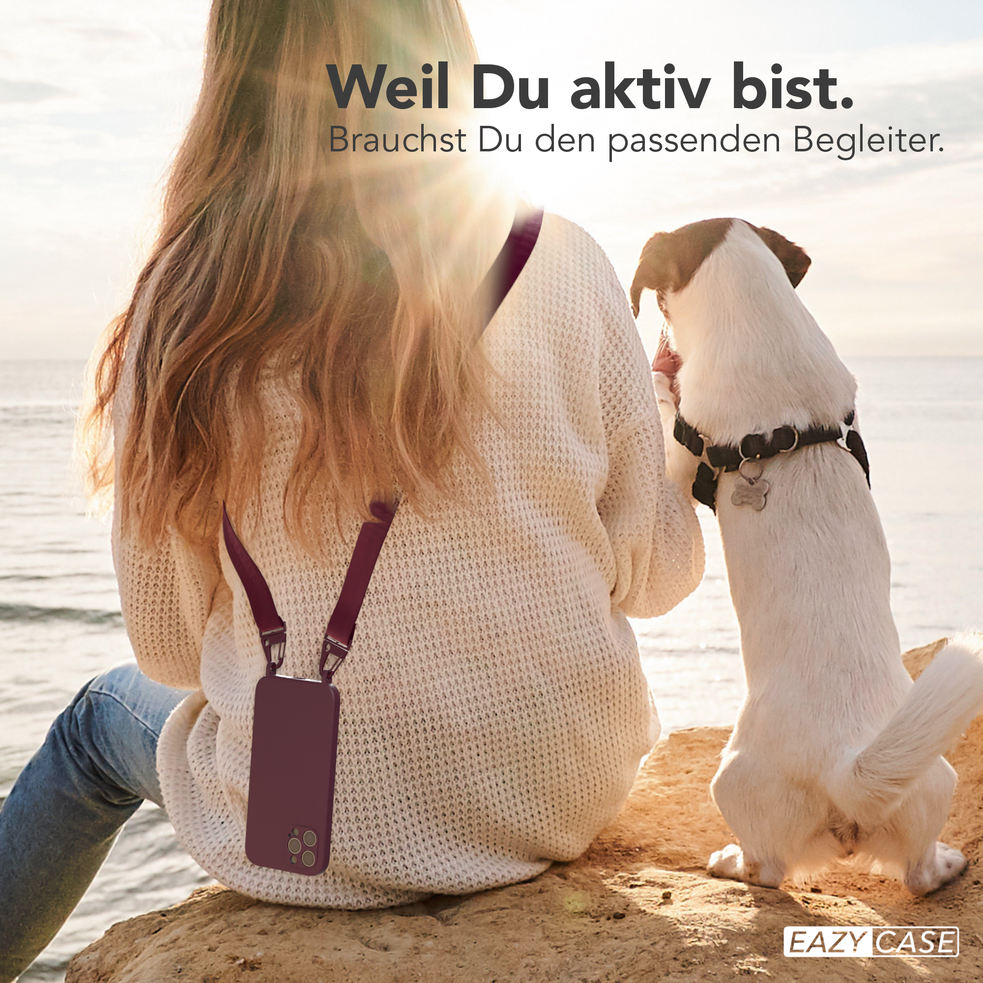 Eine Frau sitzt mit einer Handyhülle, ein Hund schaut sie an. Die Sonne scheint.