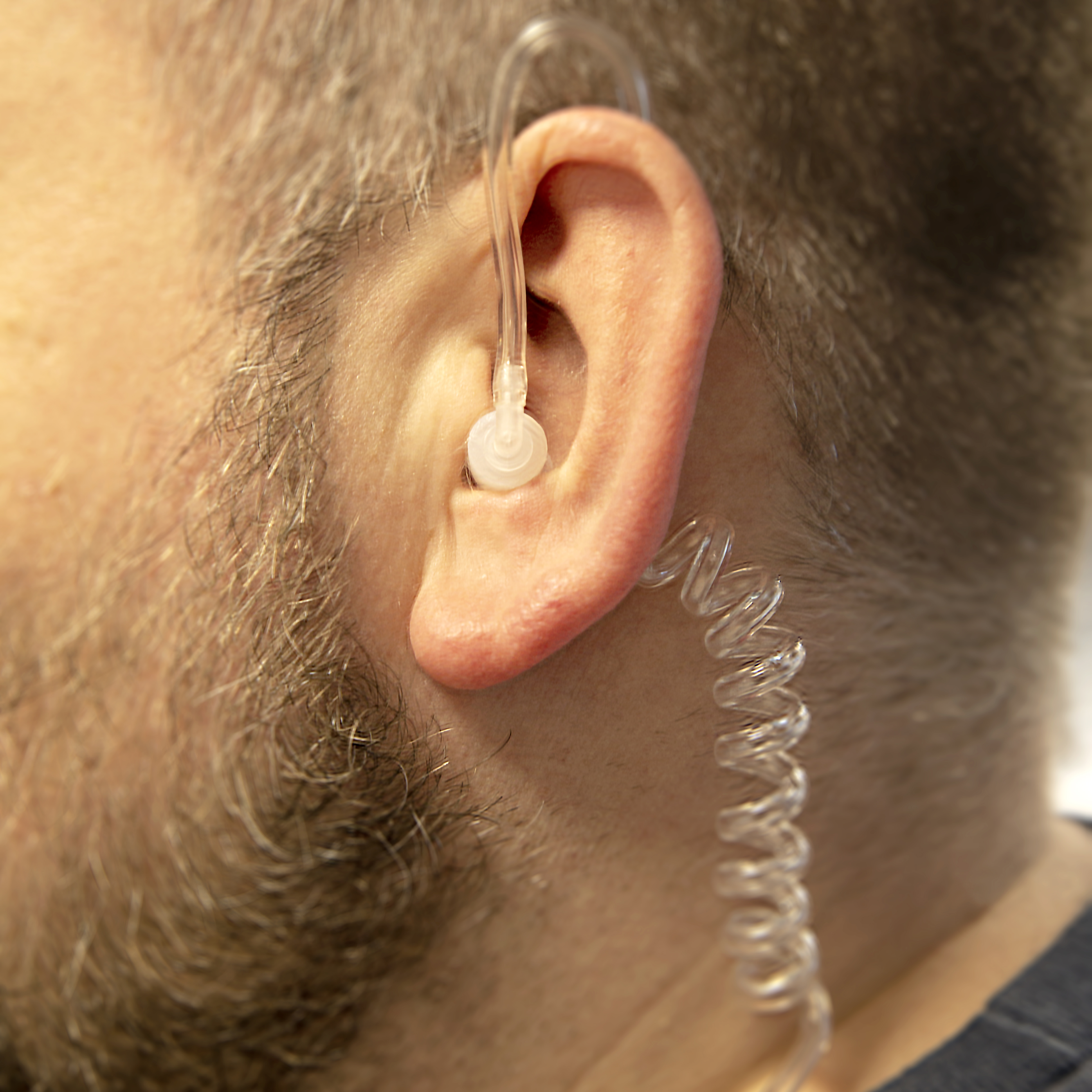Nahaufnahme eines Mannes mit Ohrhörer und Kabel. Der Mann hat einen Bart.