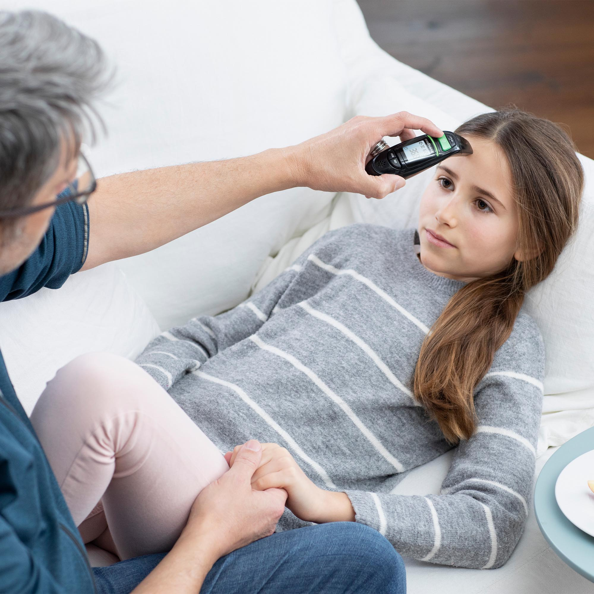 Osoba mierzy temperaturę dziecka termometrem, gdy dziecko leży.