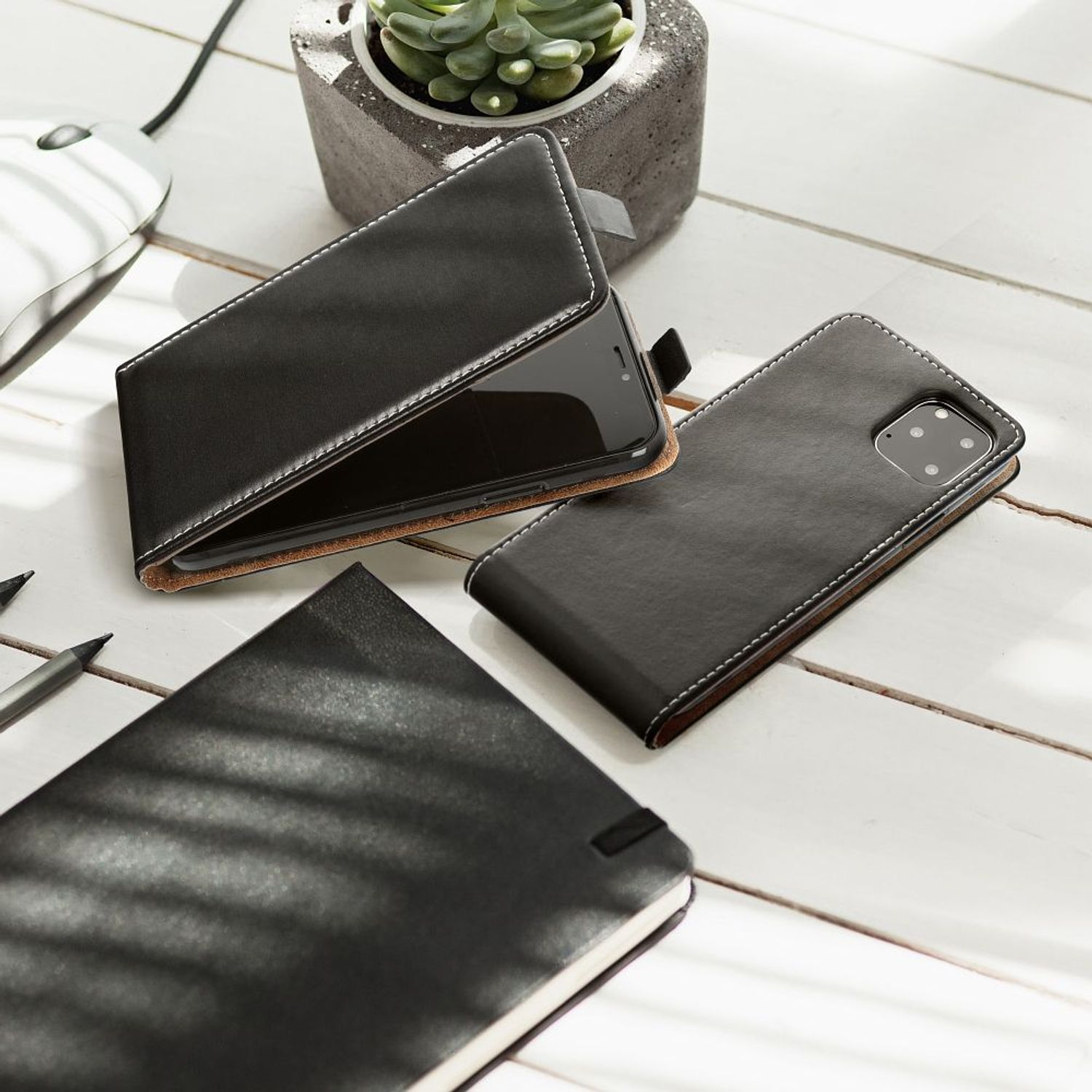 Eine schwarze Leder-Handyhülle mit Handy und Notizbuch auf einem Holztisch. Weiße Nähte.
