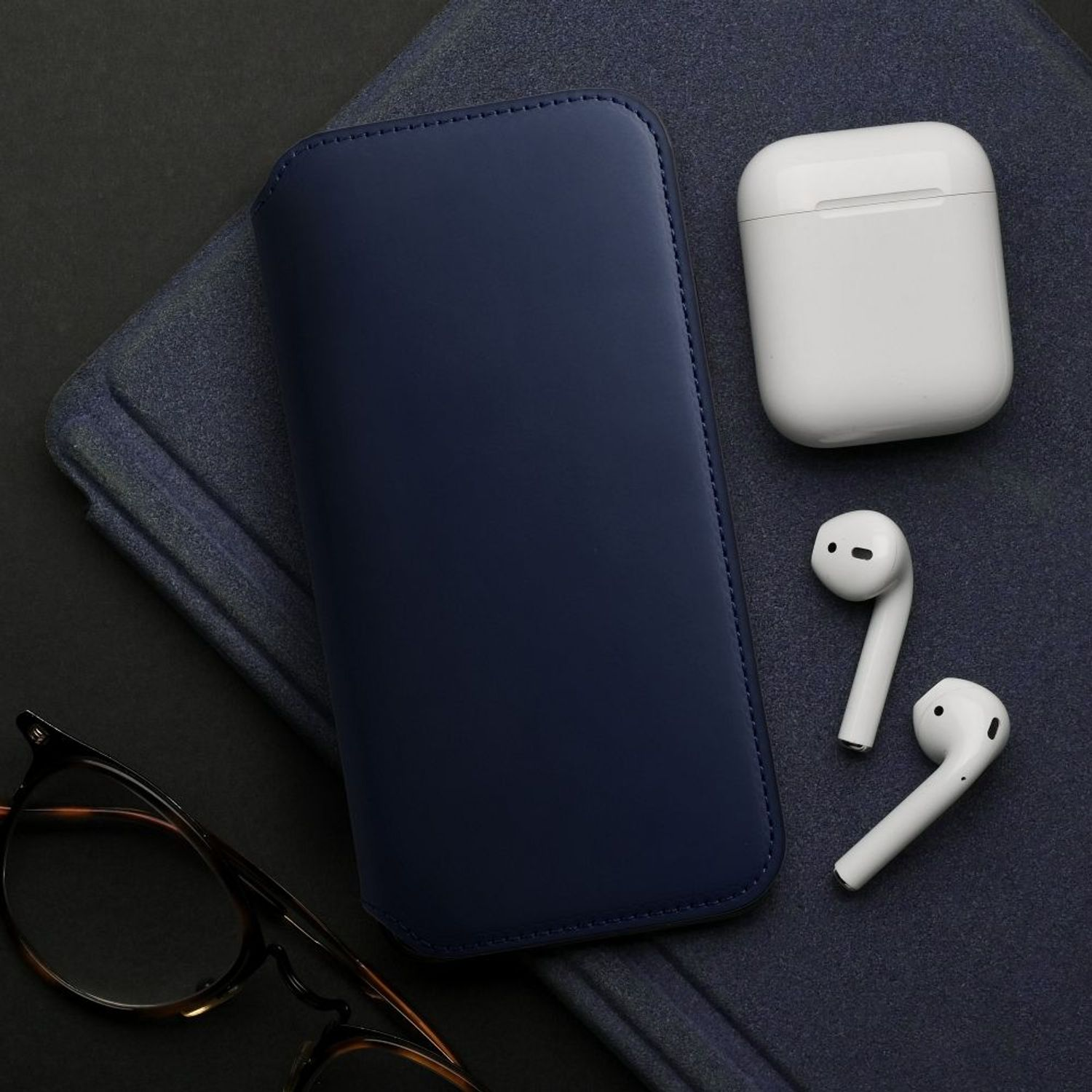Blaues Handy-Etui, AirPods und Ohrhörer auf dunkelblauem Untergrund mit Brille.