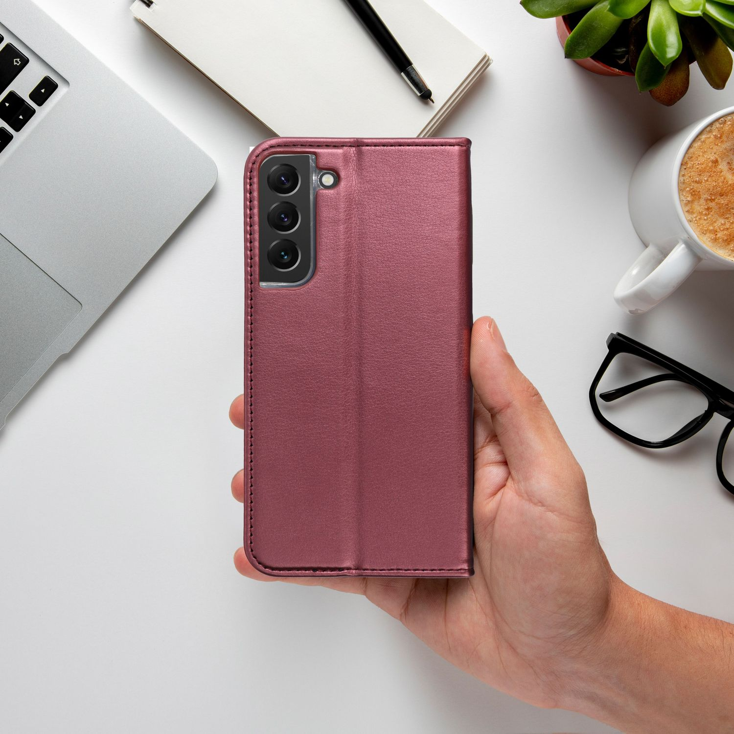 Eine Hand, die eine pinkfarbene Handyhülle mit einem Telefon darin auf einem weißen Tisch hält.