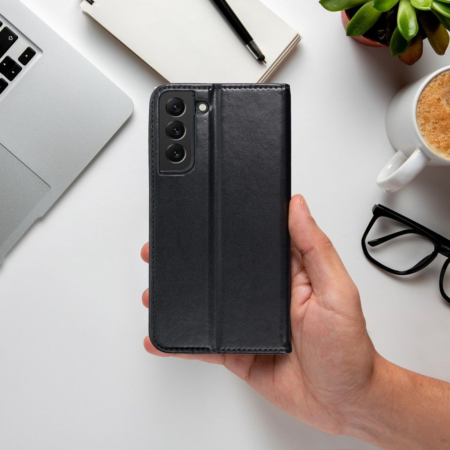 Eine schwarze Handyhülle hält ein Telefon. Die Hülle liegt auf einem Schreibtisch mit Laptop und Brille.