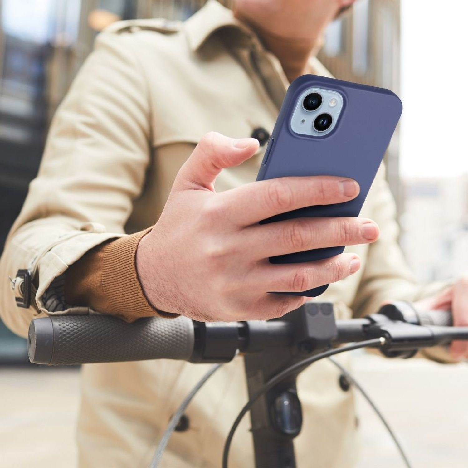 Eine Person hält ein blaues Telefon vor einem Roller. Die Person trägt einen beigen Mantel.