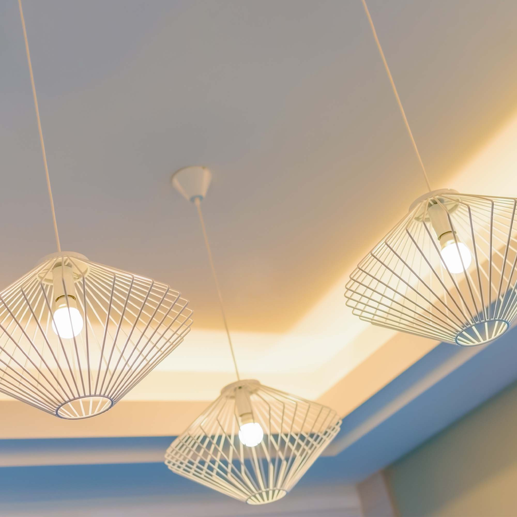 Trzy białe geometryczne lampy wiszące zwisają z białego sufitu. Każda ma żarówkę.