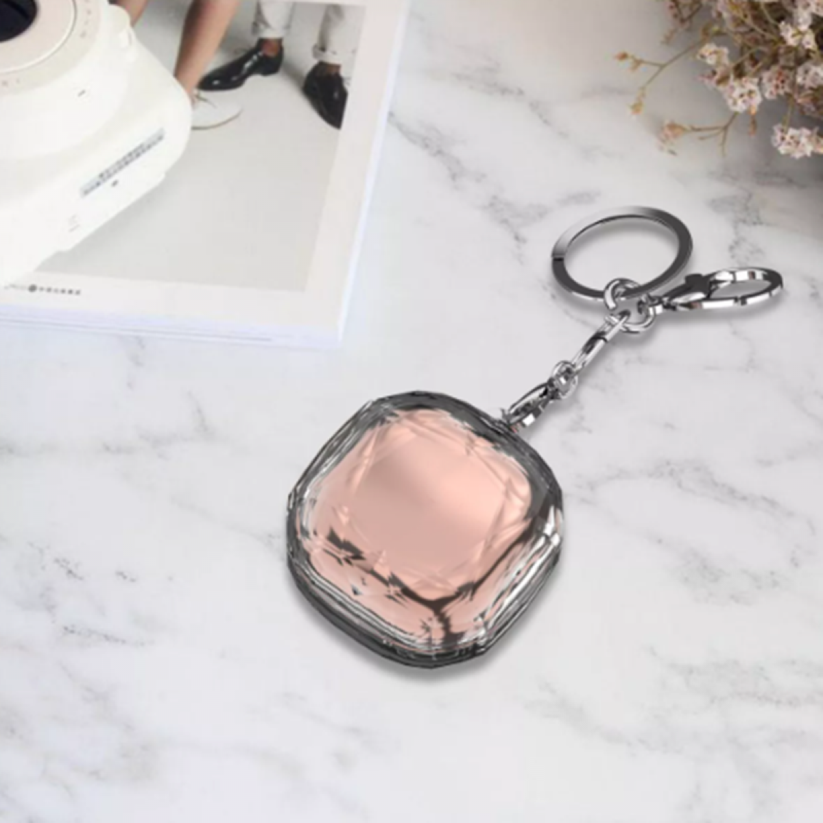 Transparenter Schlüsselanhänger mit einem rosa Quadrat, auf Marmor, und eine weiße Kamera.