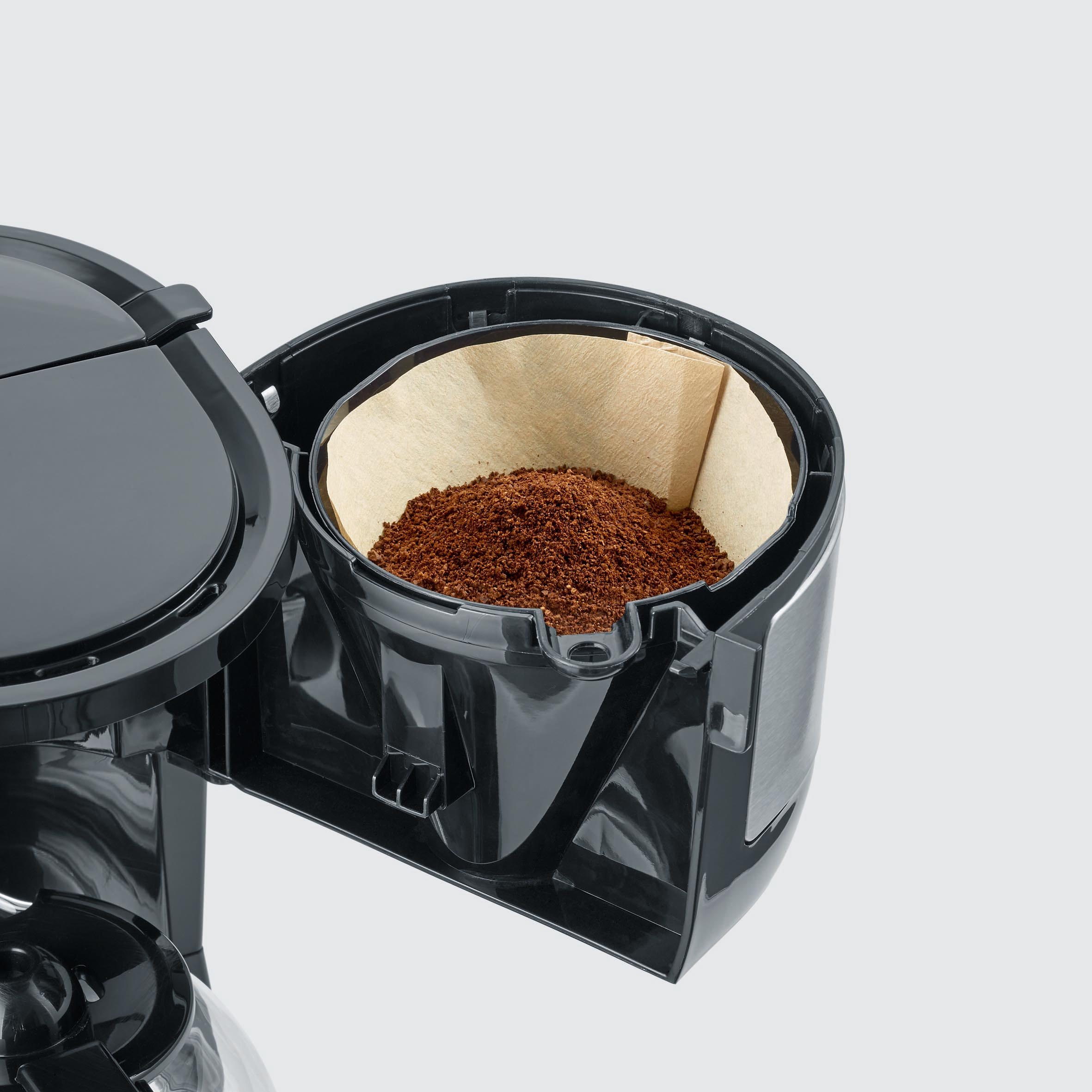 Une cafetière avec un filtre rempli de café moulu. La machine est noire et ouverte.