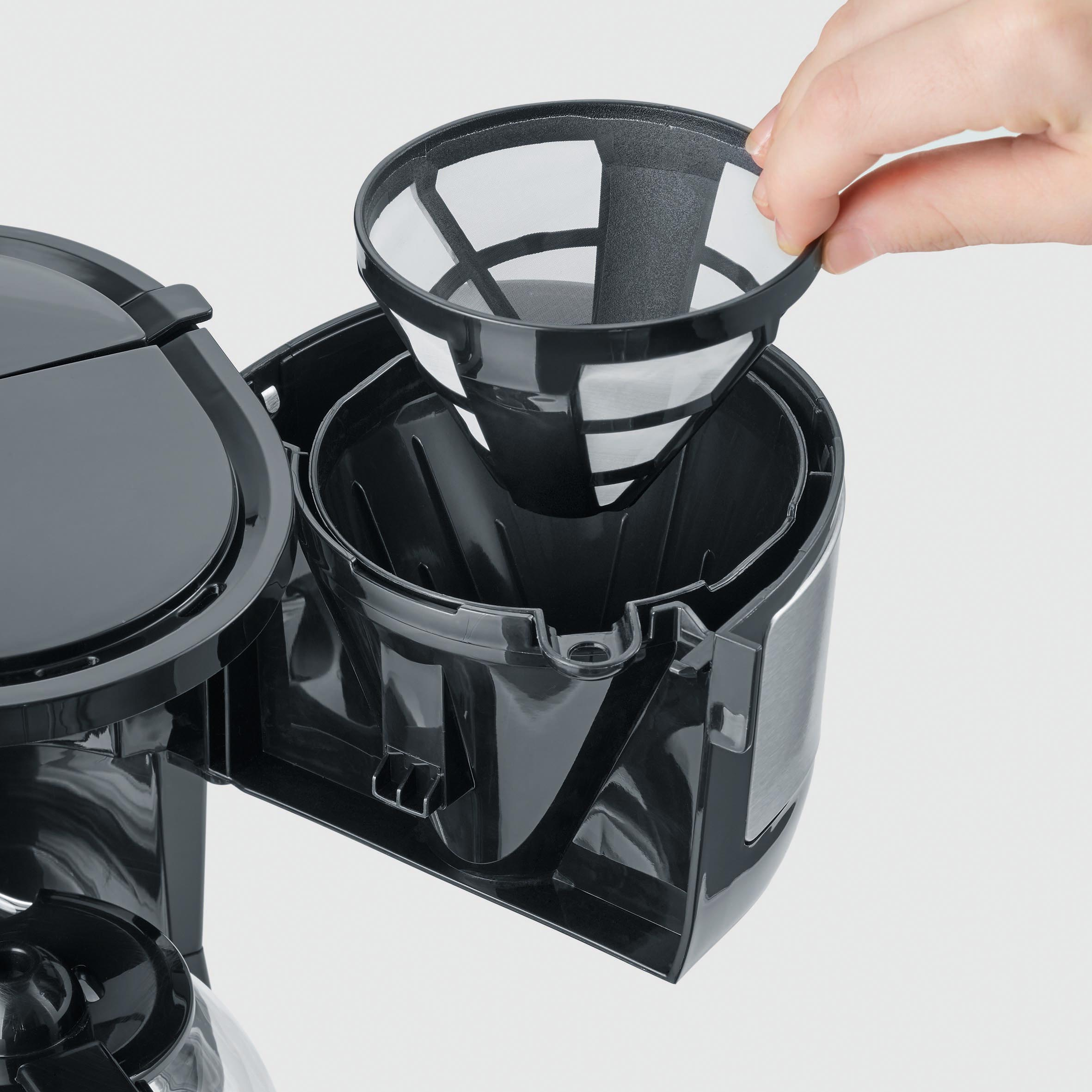 Une main place un filtre dans une cafetière noire. Le filtre est blanc.