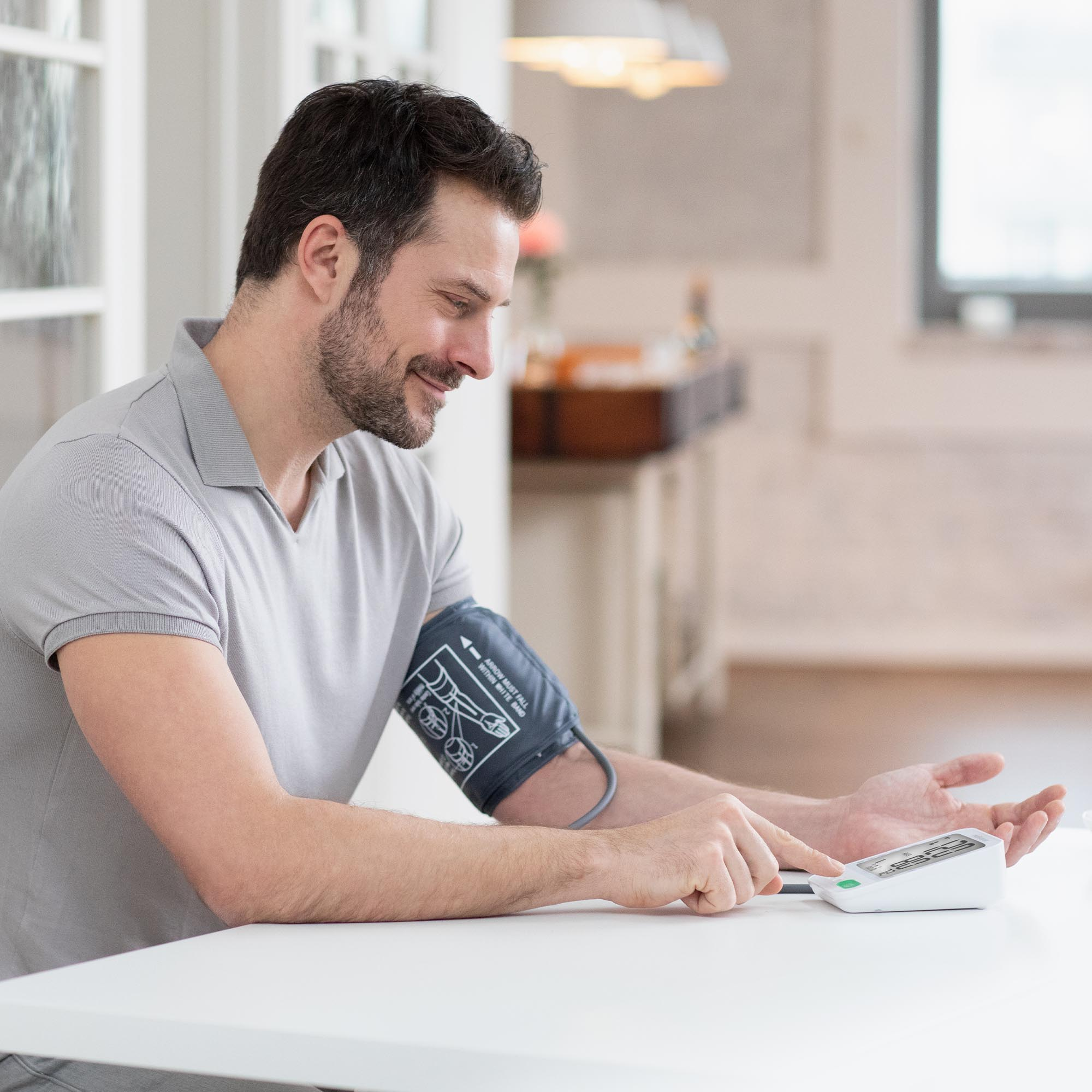 Mężczyzna mierzy ciśnienie krwi. Siedzi przy białym stole.